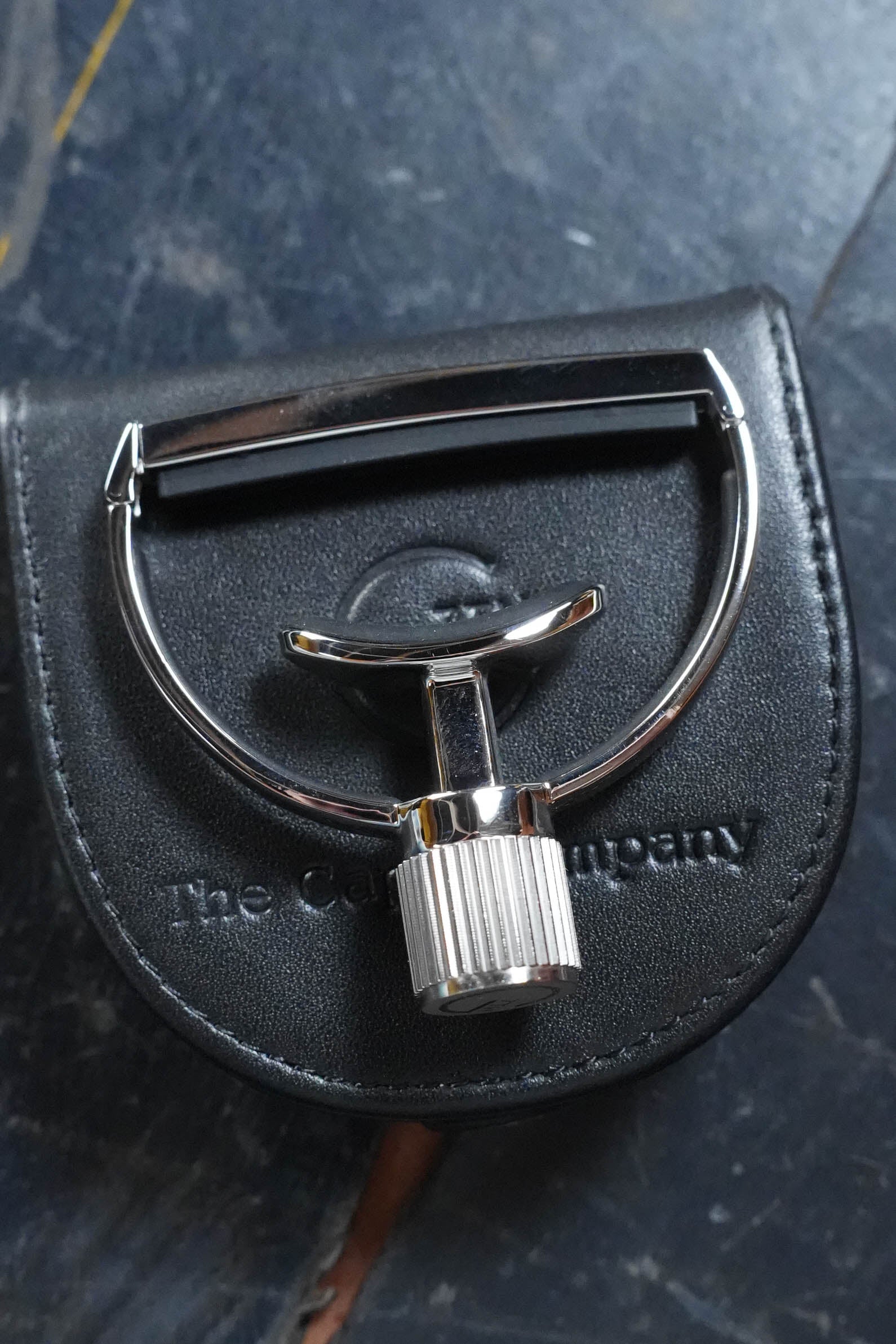 A shiny metal travel razor sits on a black embossed leather case beside the G7th Heritage Guitar Capo S1 Standard Neck Width by The Acoustic Shoppe, both reflecting modern style against a dark background.