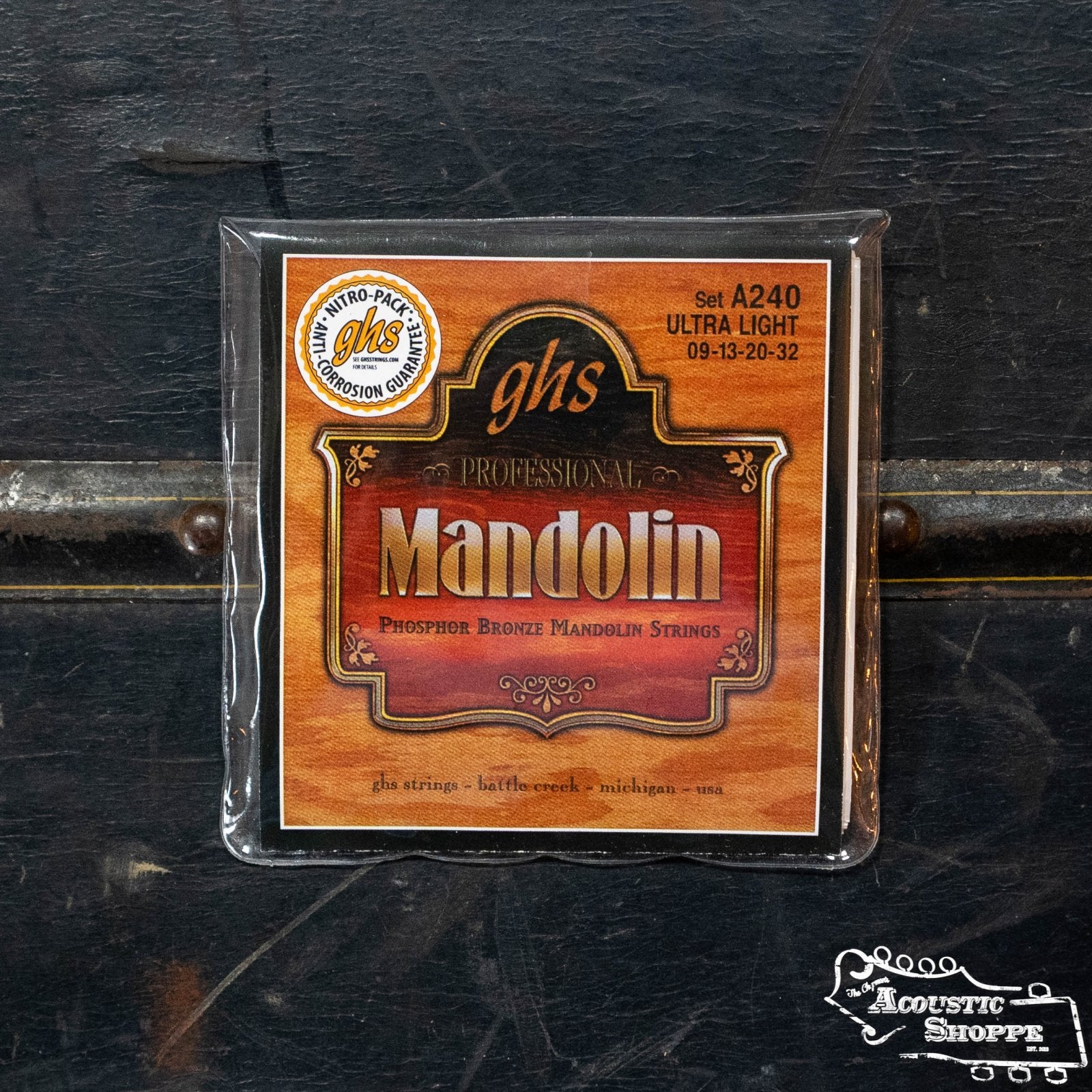 A set of GHS A240 Phosphor Bronze Loop End Mandolin Strings - Ultra Light, known for their bright, articulate tone, is shown on a dark wooden surface with The Acoustic Shoppe logo in the corner.
