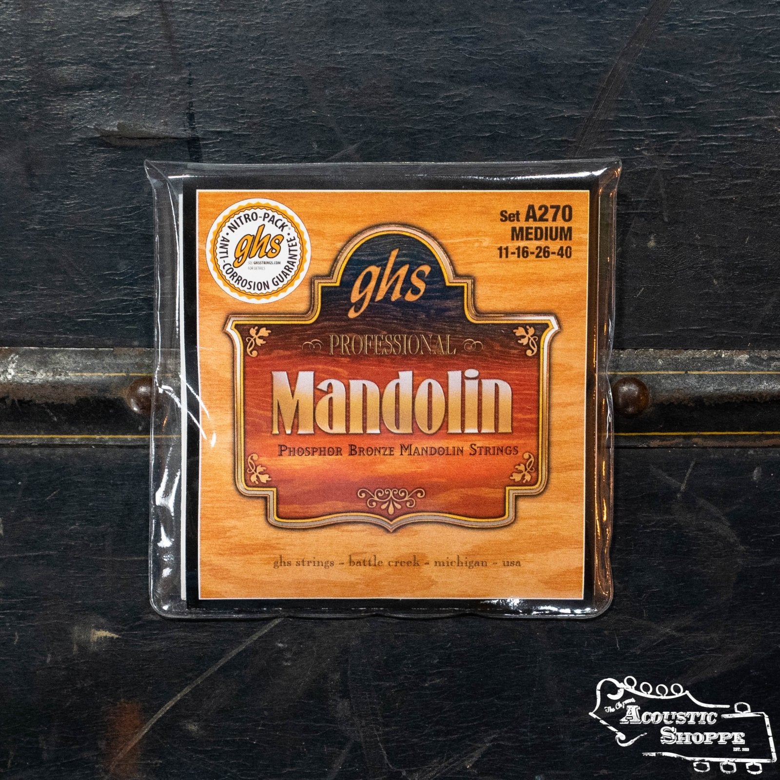 A pack of GHS Strings Phosphor Bronze Loop End Medium Mandolin Strings (A270) is shown on a dark wooden surface with The Acoustic Shoppe logo in the lower right. Ideal for musicians seeking quality medium mandolin strings.