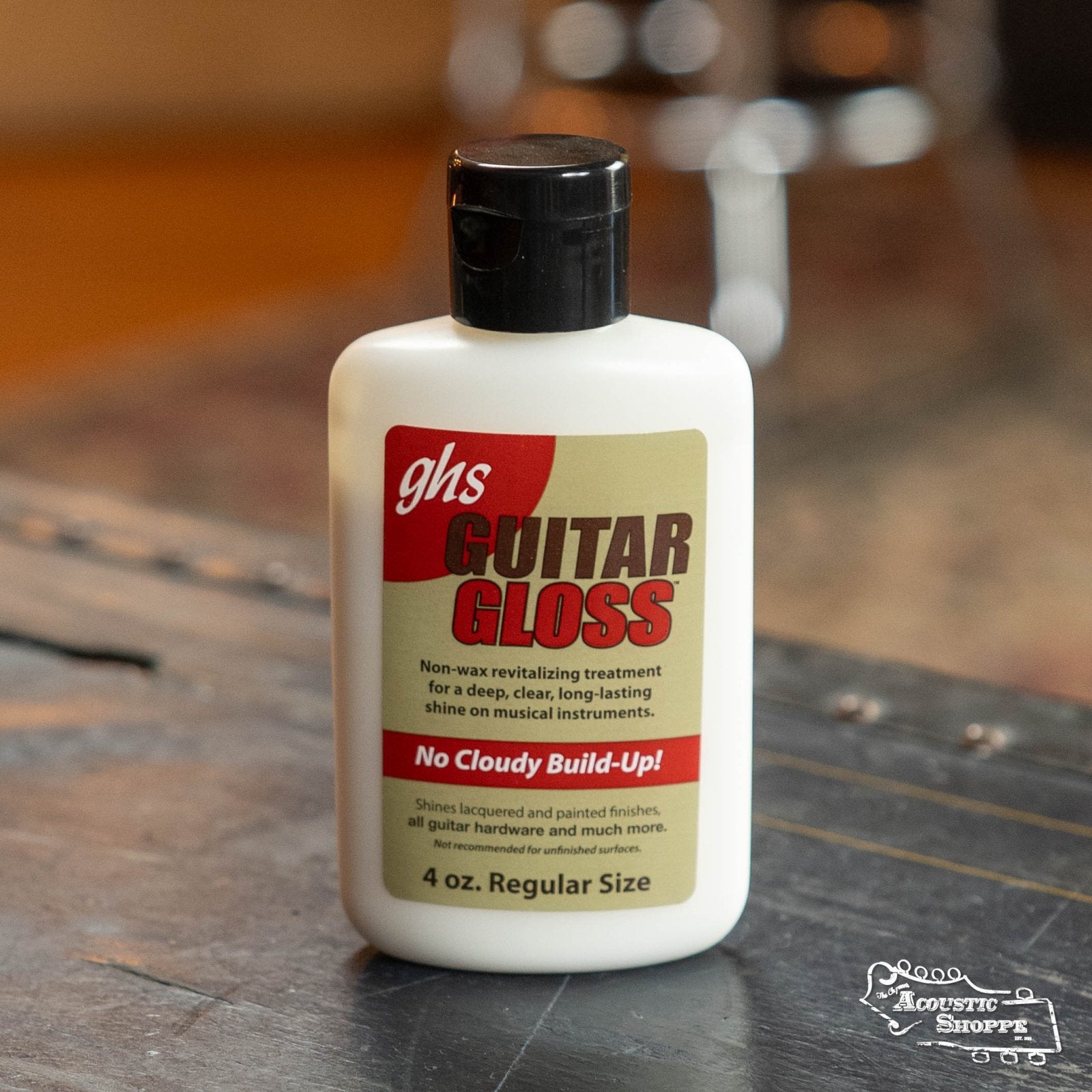 A bottle of GHS Strings Guitar Gloss Polish 4oz (A92) sits on a wooden surface. The label reads “Guitar Gloss” and describes it as a non-wax instrument polish for a deep, clear shine without cloudy buildup.