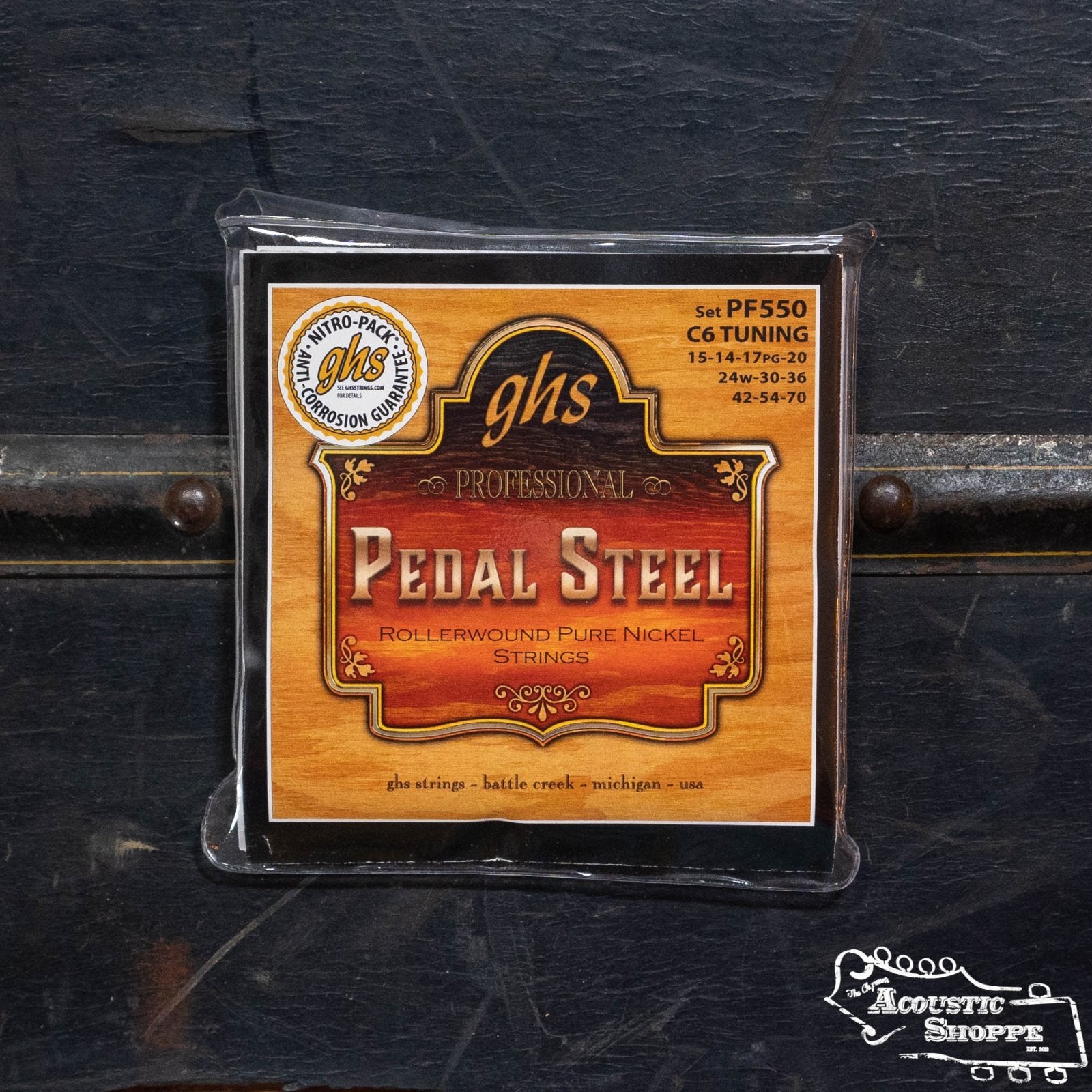 A pack of GHS Strings Steel Pedal C6th Tuning (PF550) by GHS Strings is displayed on a dark wooden surface, featuring an orange and brown label with product details and a Nitro-Pack logo.