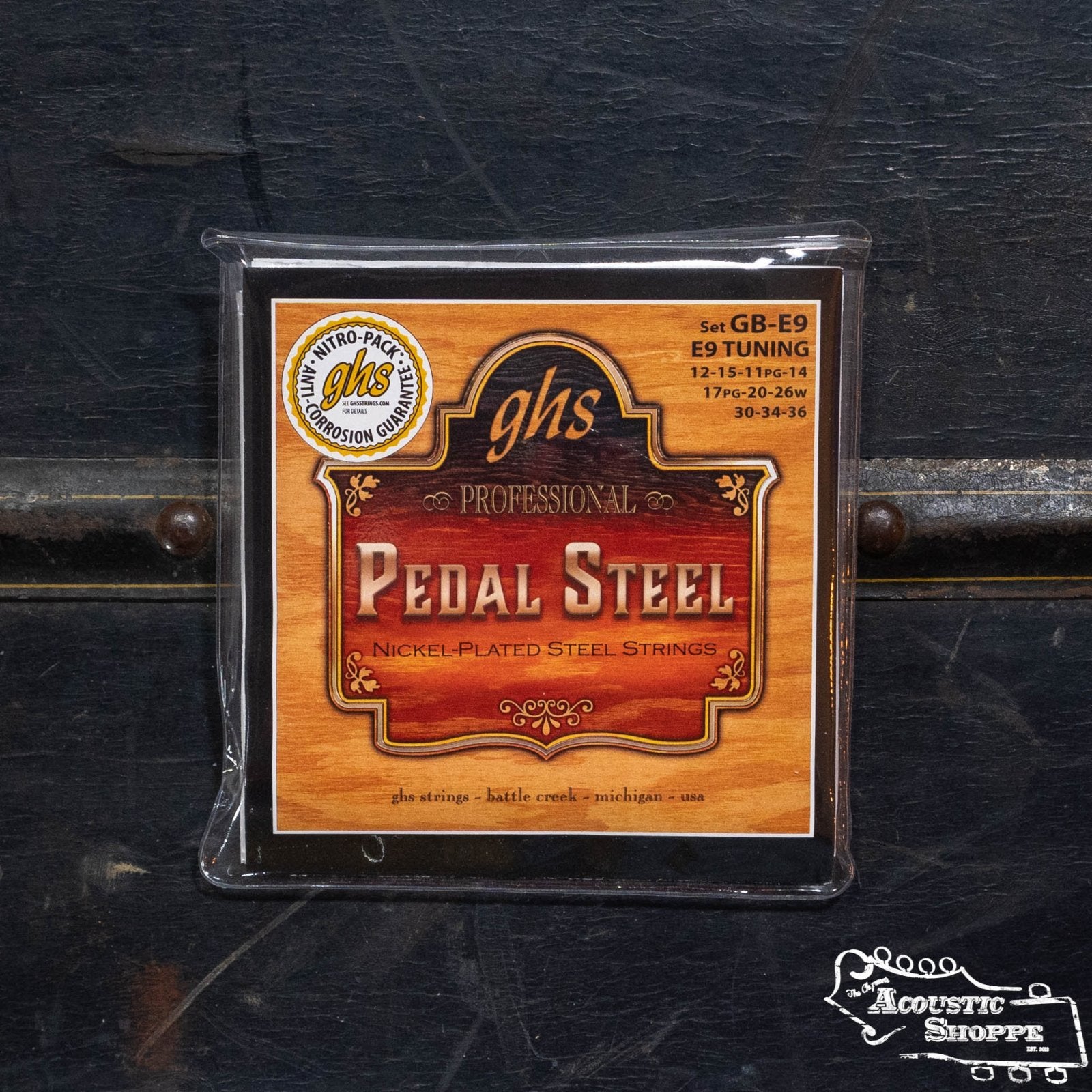 A pack of GHS Strings GB-E9 Pedal Steel Boomers E9 Tuning, nickel-plated steel guitar strings, is shown in plastic packaging with a woodgrain design and yellow/red text on a dark surface.