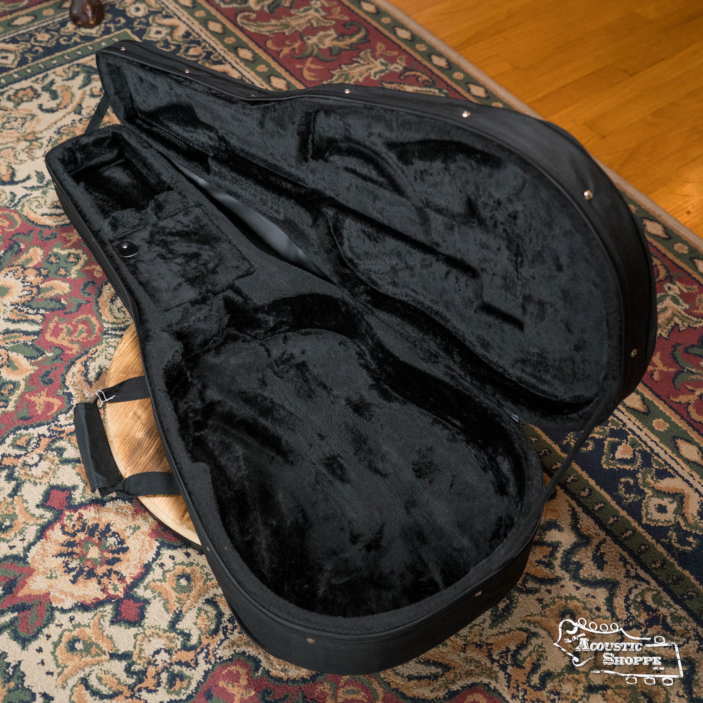 A Guardian CG-012-D Foam Guitar Case for dreadnought guitars, featuring high-density foam padding and a plush interior, sits open and empty on a patterned rug and wood floor. The Acoustic Shoppe logo appears in the lower right corner.