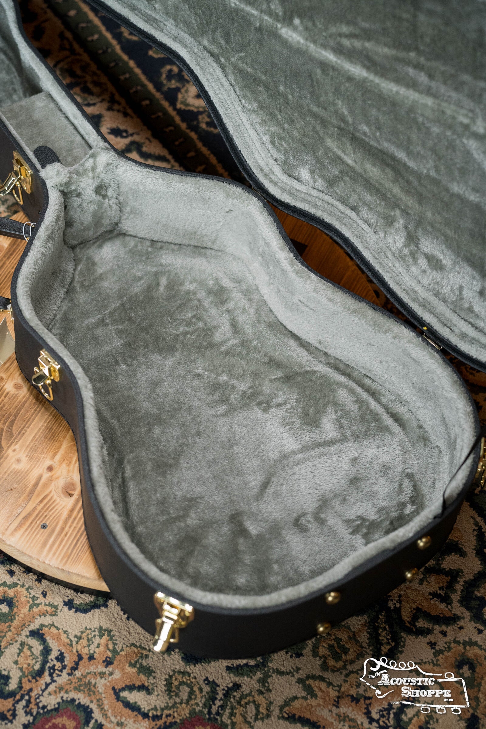 The Guardian CG-018-D Economy Archtop Case Dreadnought by Guardian is open and empty on a patterned rug, revealing its plush grey interior, soft lining, and secure metal latches.
