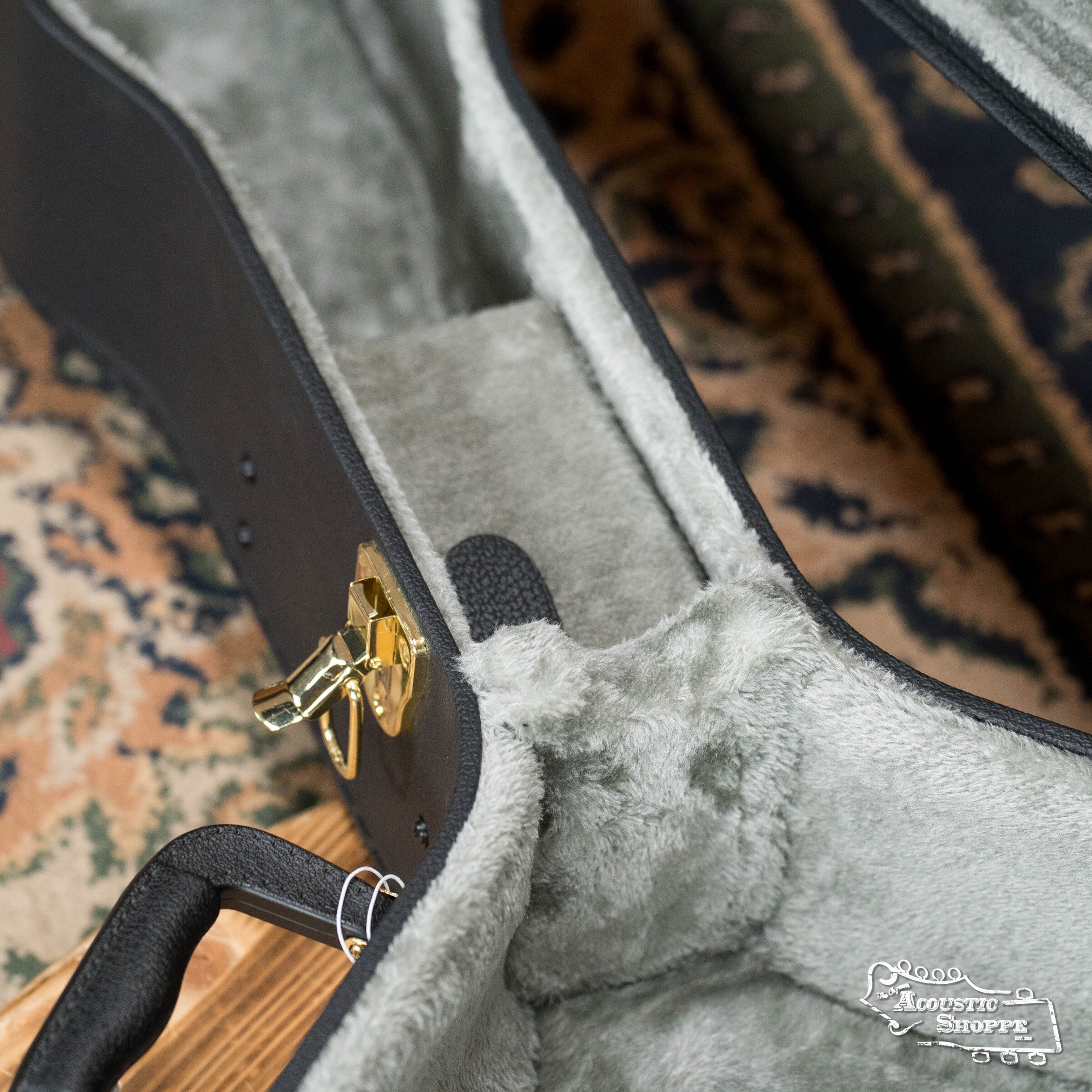 A Guardian CG-018-D Economy Archtop Case Dreadnought with soft gray fur-like lining, gold latch, and handle sits on a patterned rug. The Acoustic Shoppe logo is visible in the bottom right corner.