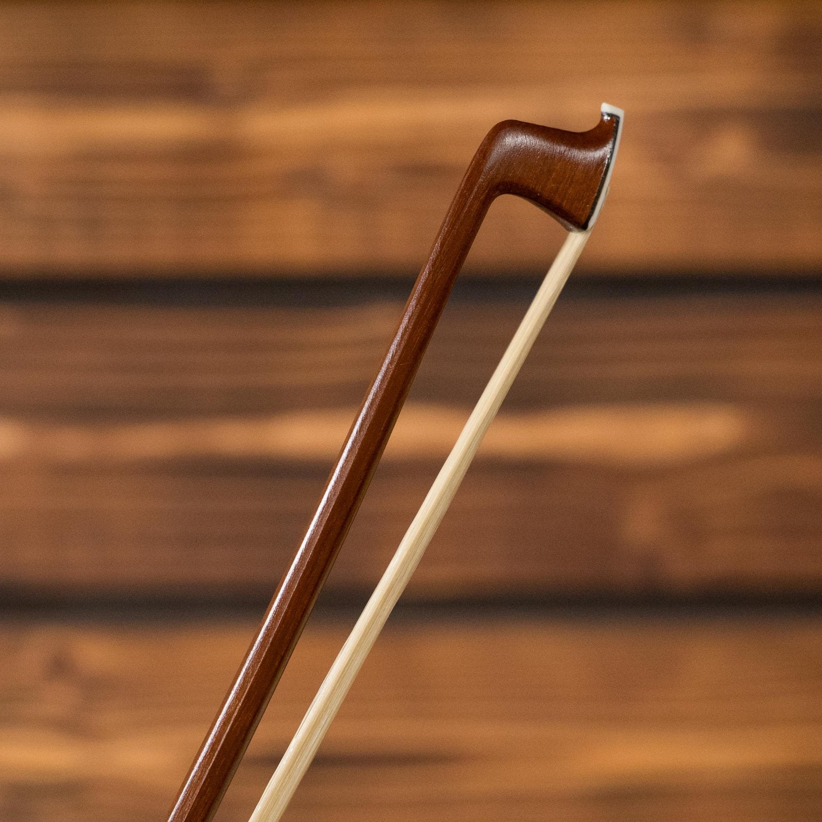 A close-up of the tip of a Howard Core 1076VN 4/4 Violin Bow by Howard Core, shown against a blurred wooden background.