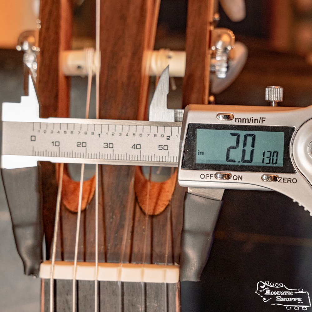 Close-up of a digital caliper measuring the width (2.0 cm) of the nut on a Cordoba C3M Red Cedar/Mahogany Classical Guitar #8691, with strings and tuning pegs visible in the background.