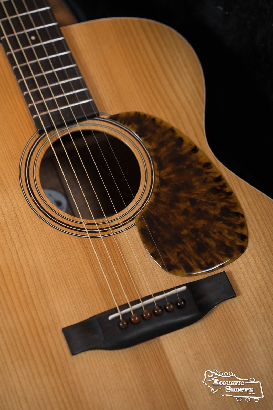 Close-up of a Hinde Adirondack/Quilted Sapele OO 14-Fret Acoustic Guitar #6 body with an Adirondack spruce top, quilted sapele back and sides, tortoiseshell-patterned pickguard, and The Acoustic Shoppe logo in the lower right corner.