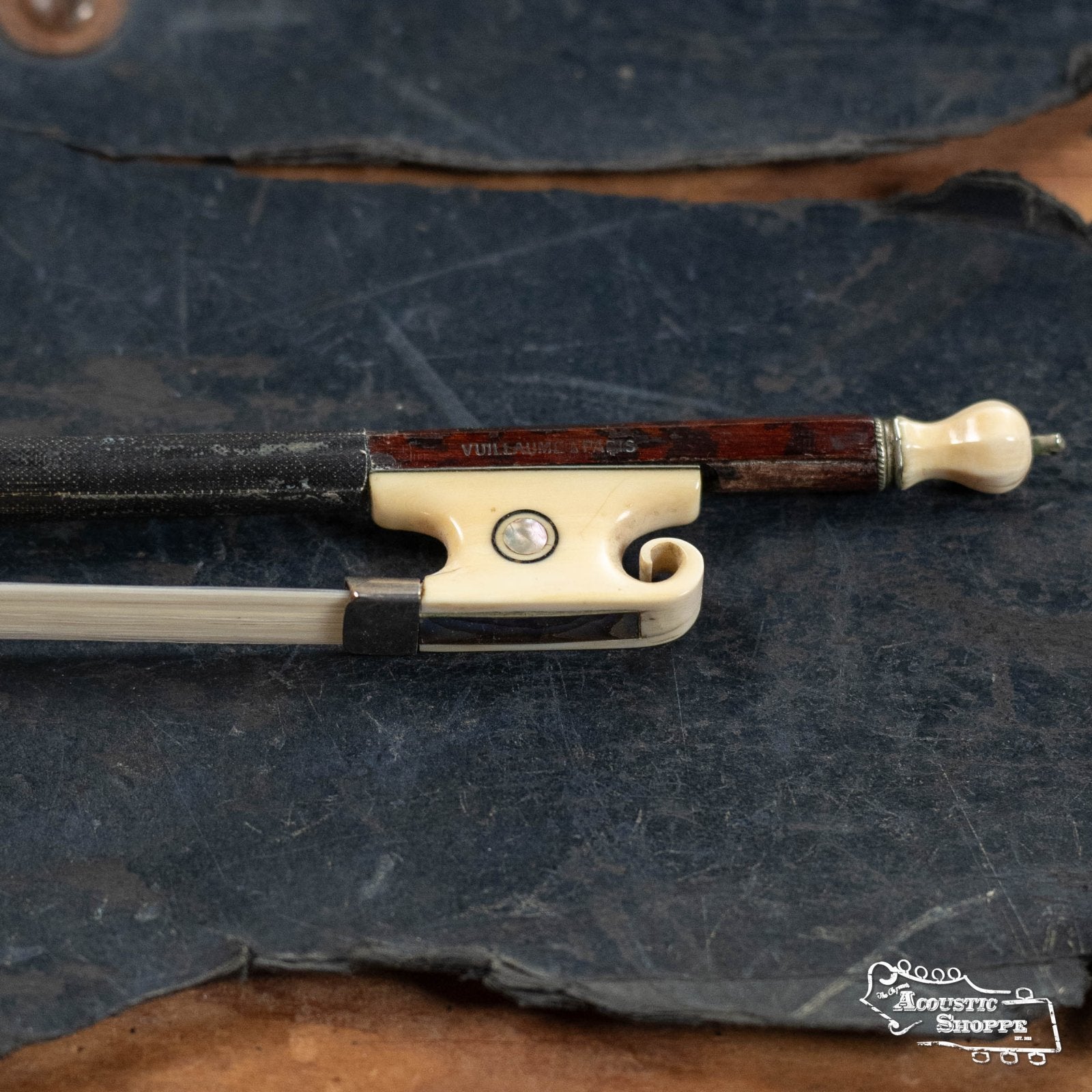 A close-up of a (Used) Horse Hair Fiddle Bow (2) by Used Items, featuring a cream-colored frog and screw engraved with Vuillaume, rests on a dark textured surface, with The Acoustic Shoppe logo in the bottom right corner.
