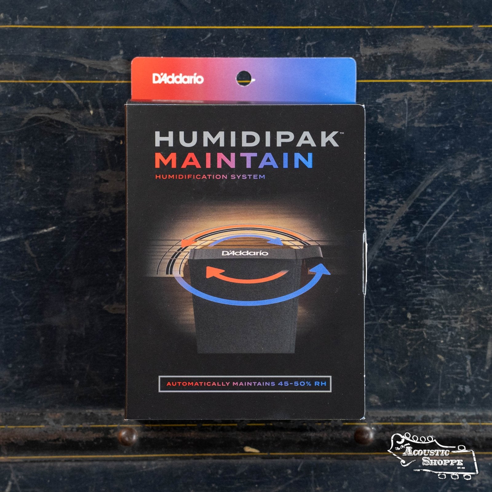 A box of the DAddario PW-HPK-01 Humidipak Starter Kit Two-Way Humidification System sits on a dark, worn wooden surface. The packaging features bold text and a circular graphic noting 45-50% humidity control for guitars.