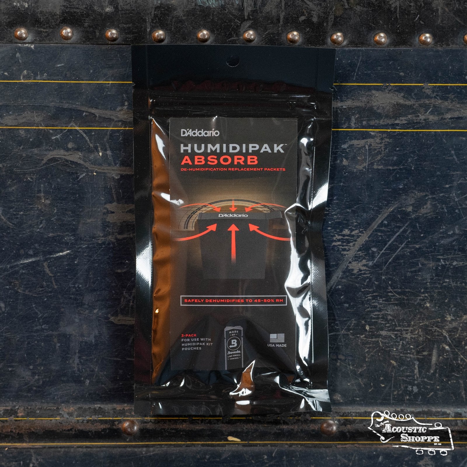 A DAddario Absorb Replacement 3-Pack is shown on a blue, weathered metal surface with visible rivets and arrows. The Acoustic Shoppe logo is visible in the bottom right corner.