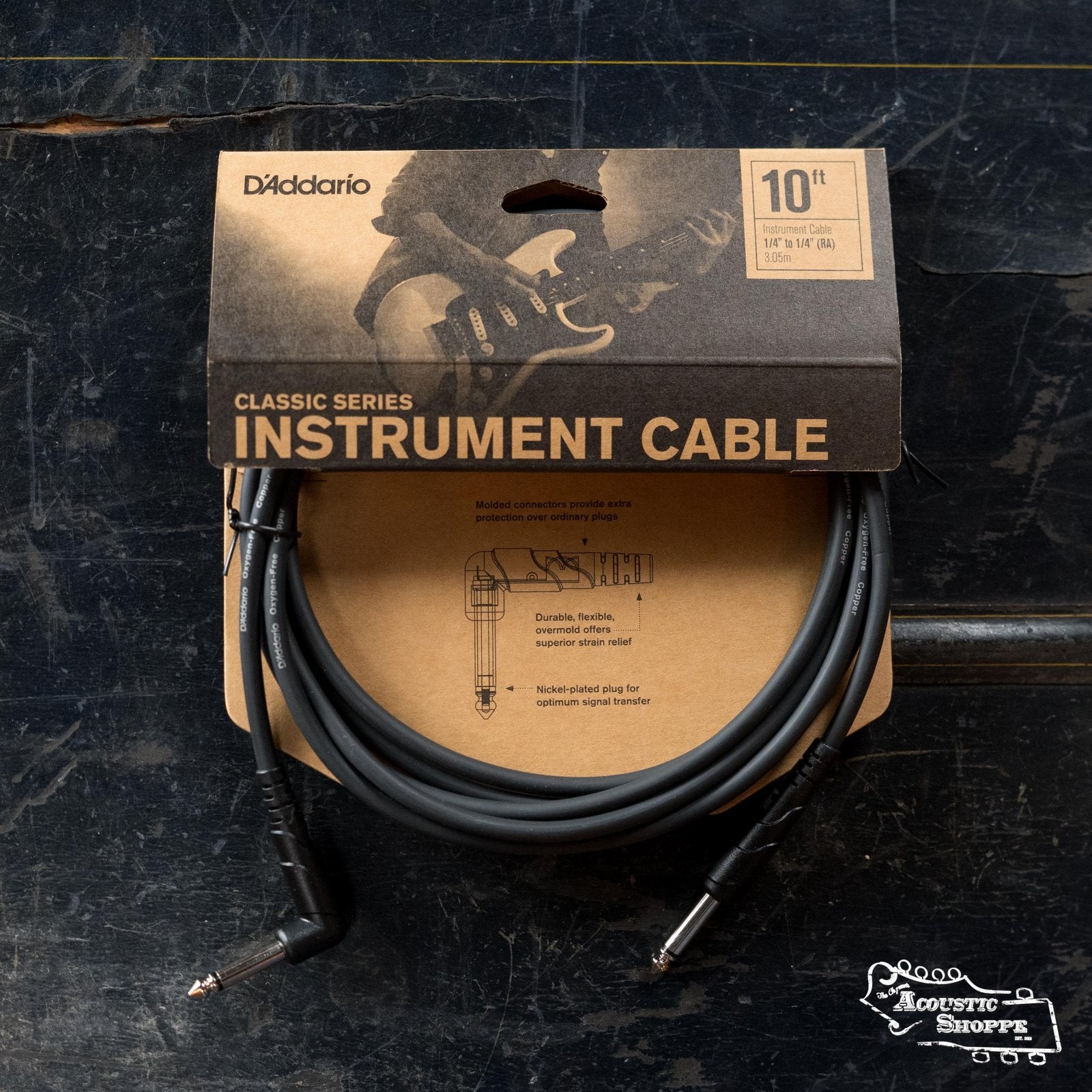 A D'Addario PW-CGT-10 Classic Series 10-foot instrument cable by D’Addario, packaged in brown and black with a guitarist graphic, lies coiled on a dark textured surface.