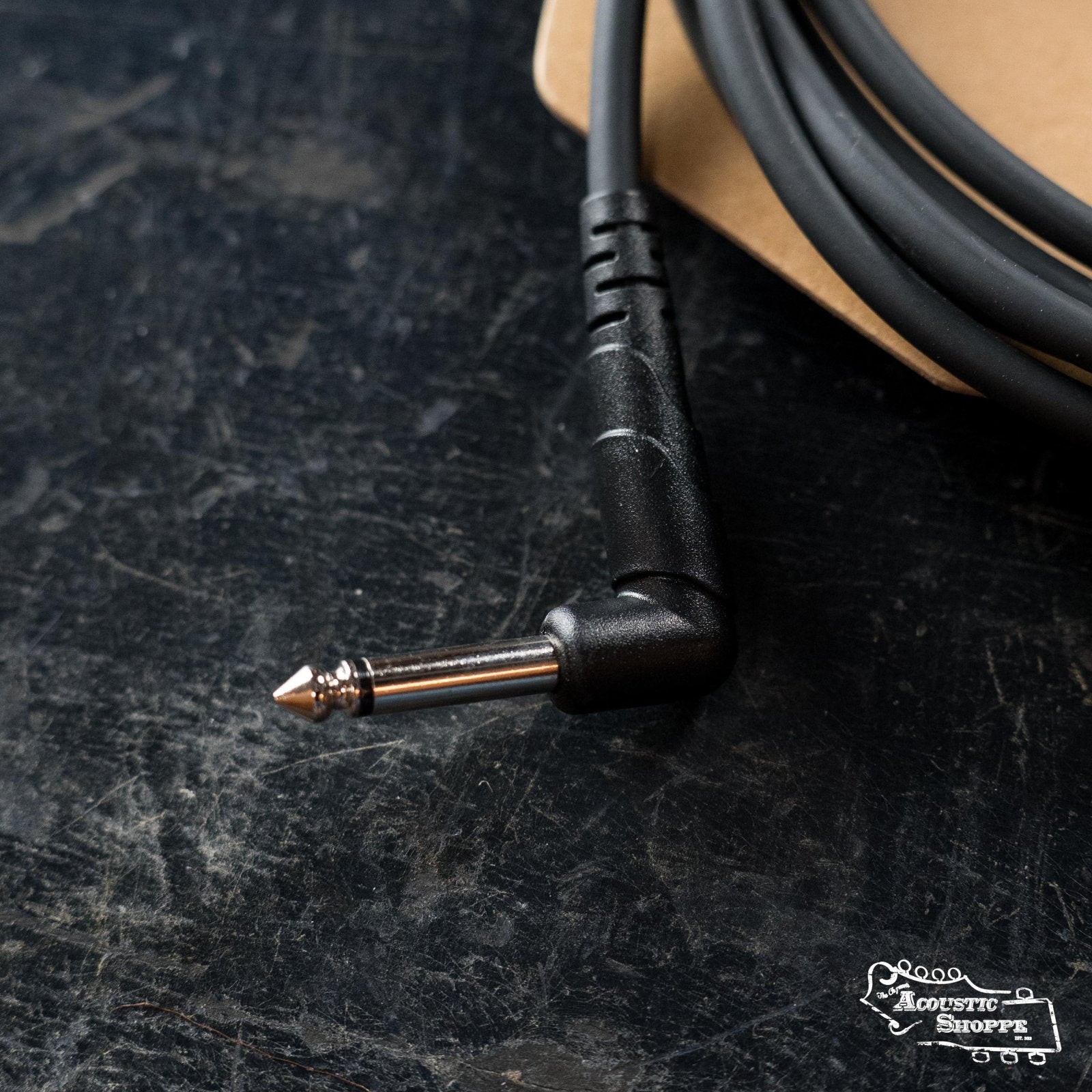 A close-up of the D'Addario PW-CGT-10 Classic Series 10-foot instrument cable with a right-angle 1/4-inch plug lies on a dark surface. Made with oxygen-free copper, some coiled cable and the cardboard packaging are also visible.