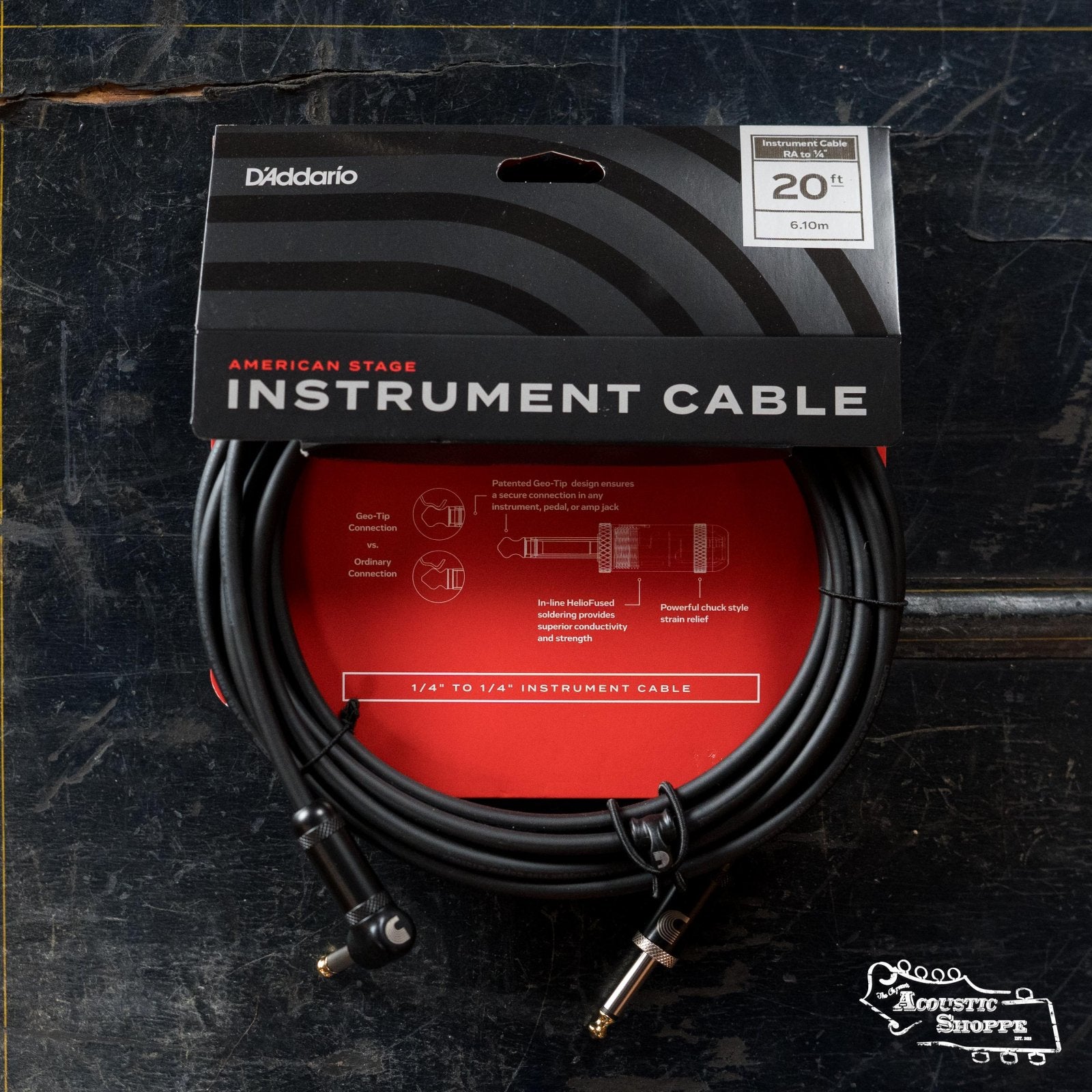 A D'Addario American Stage Instrument Cable Right to Straight 20 feet (PW-AMSGRA-20) is shown in its packaging on a dark surface, with product details and capacitance diagrams visible on the red backing card.