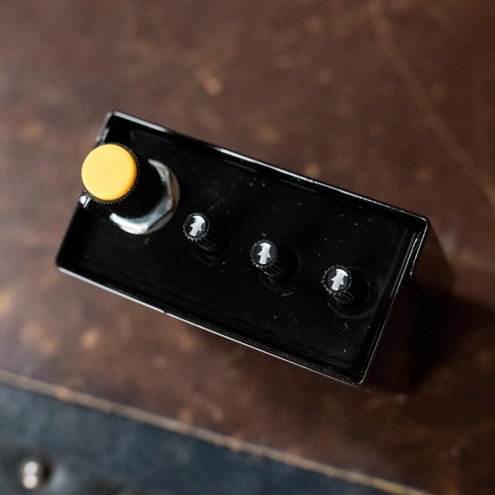 A black, rectangular K&K Sound Pure Preamp pedal with a large yellow knob and three smaller black knobs, viewed from above on a brown surface—ideal as an acoustic guitar preamp with internal gain trimmer.
