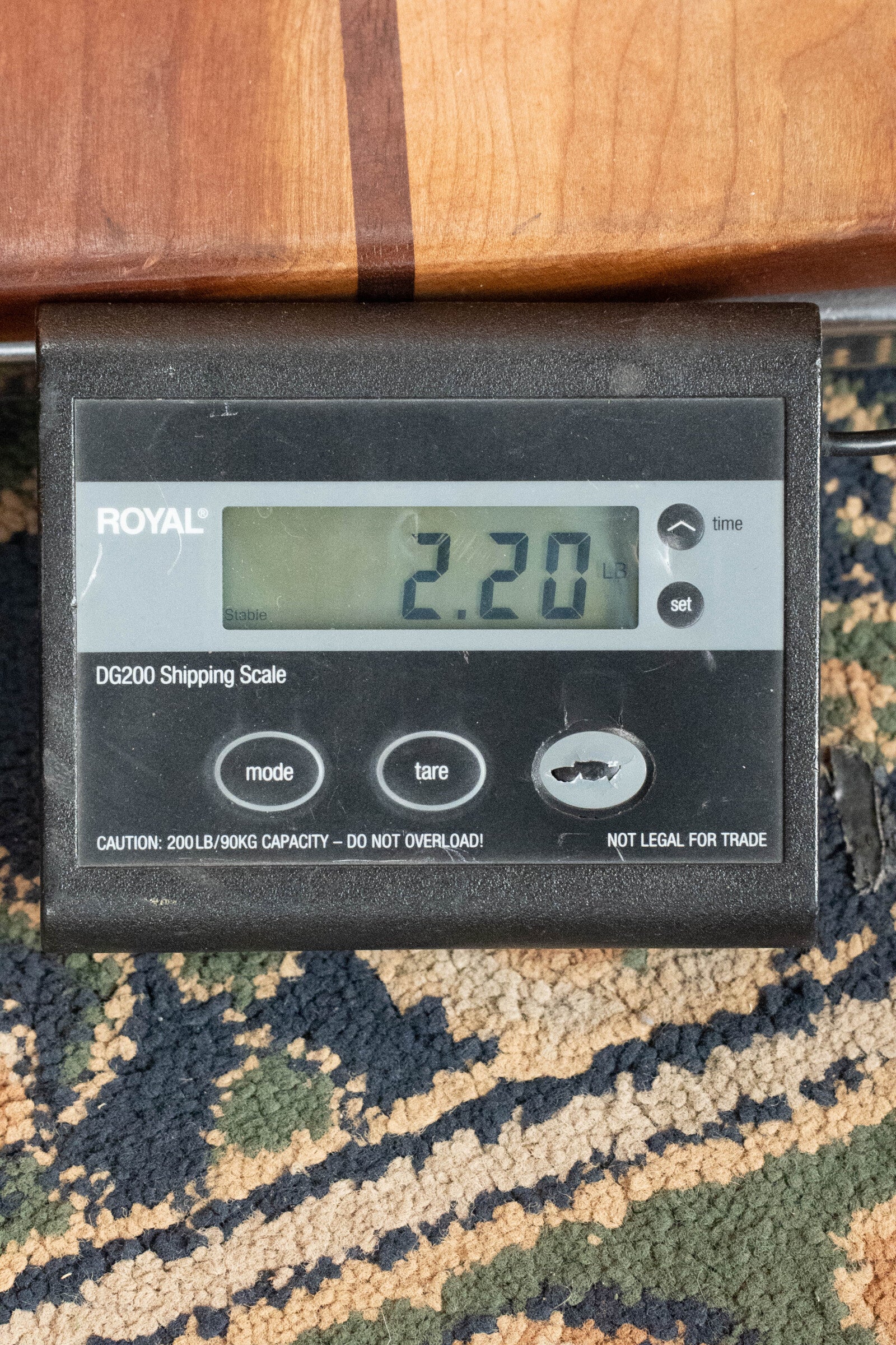 A KLOS Guitars CT_MA_DAE_EQ Full Carbon Unidirectional Black A-Style Mandolin with EQ Pickup (#4889) partially rests on a black digital shipping scale with gray buttons, showing a weight of 2.20 pounds on patterned carpet.