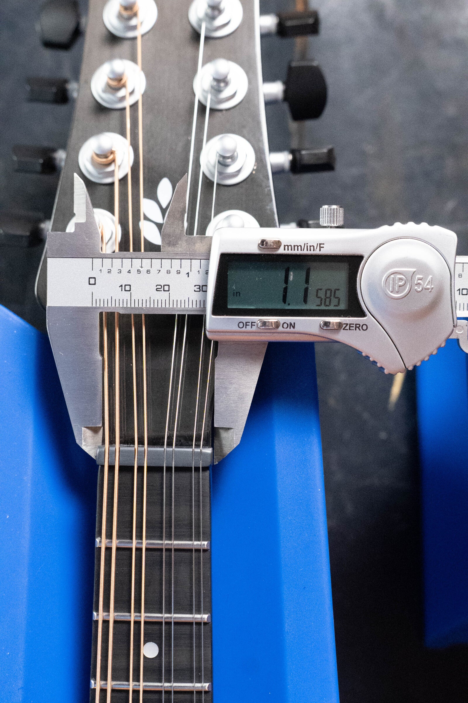 A KLOS Guitars CT_MA_DAE_EQ Full Carbon Unidirectional Black A-Style Mandolin w/KLOS EQ Pickup #4889 rests on a blue stand as a digital caliper measures its neck width near the headstock at 1.585 inches.