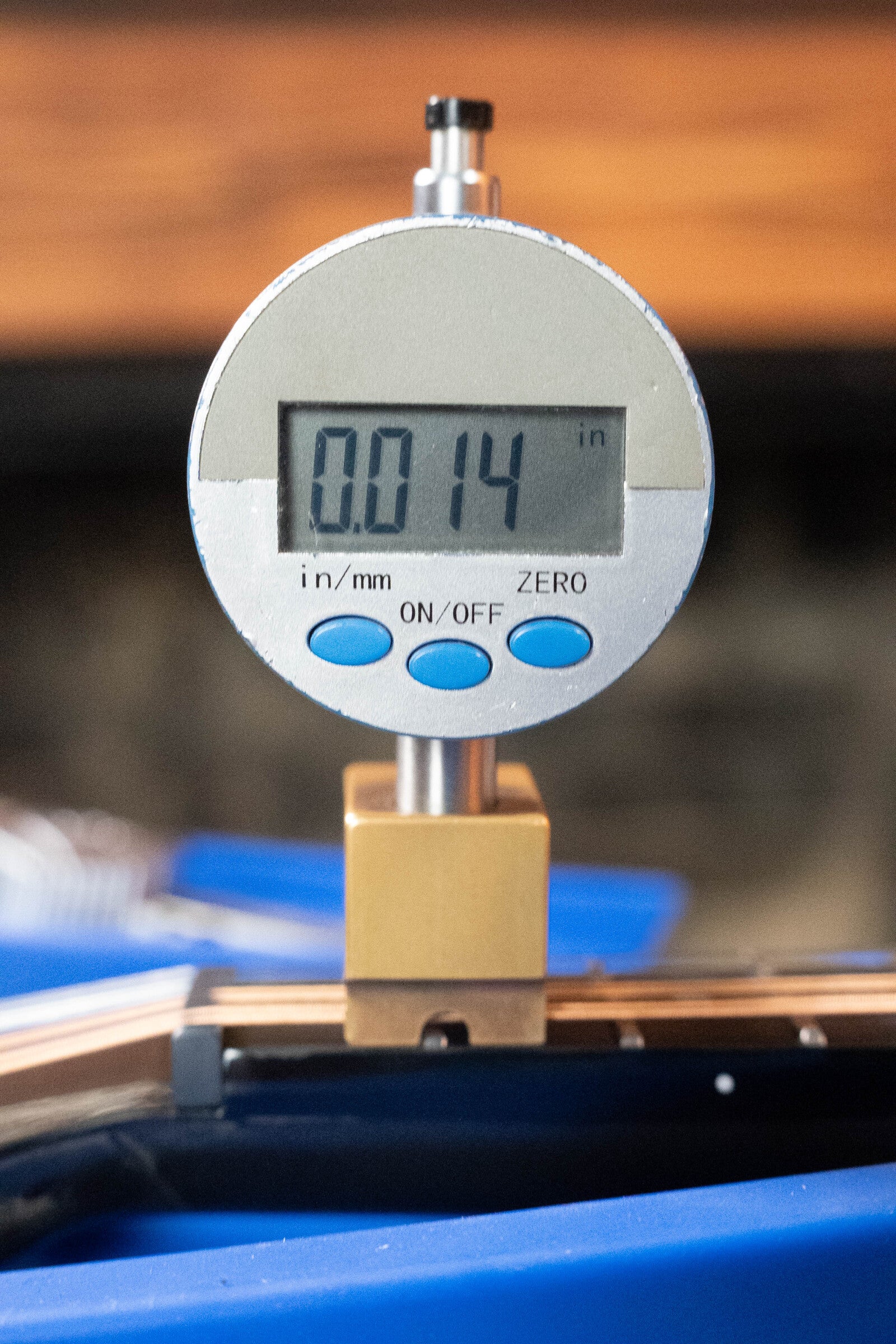 A digital caliper gauge shows 0.014 inches as it is mounted above a KLOS CT_MA_DAE_EQ Full Carbon Unidirectional Black A-Style Mandolin w/KLOS EQ Pickup #4889 by KLOS Guitars, possibly measuring its precision-crafted surface.