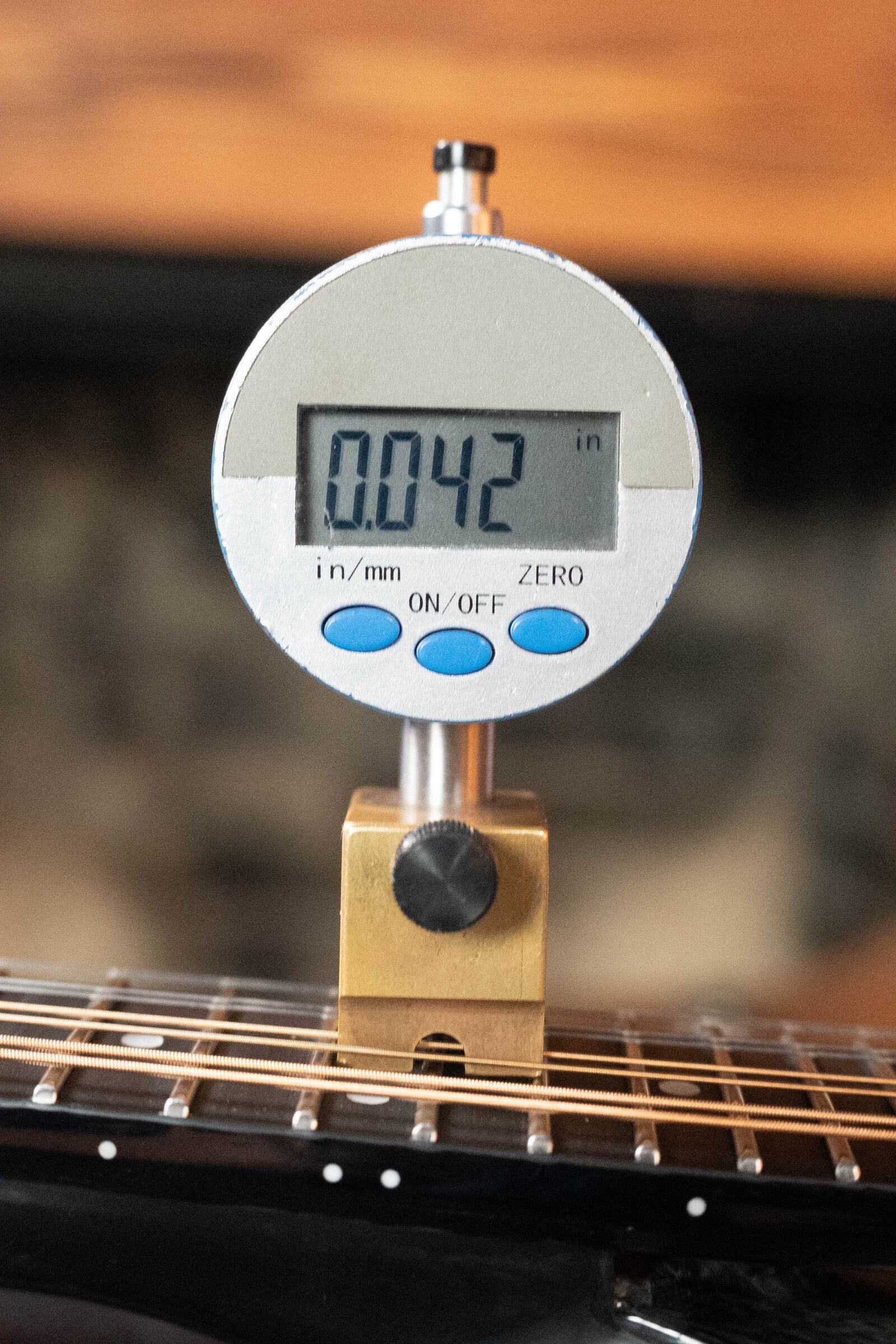 A digital gauge with blue buttons and a metallic body reads 0.042 inches on a gold block placed on the strings near the fretboard of a KLOS Guitars CT_MA_DAE_EQ Full Carbon Unidirectional Black A-Style Mandolin (#4889) with KLOS EQ Pickup.