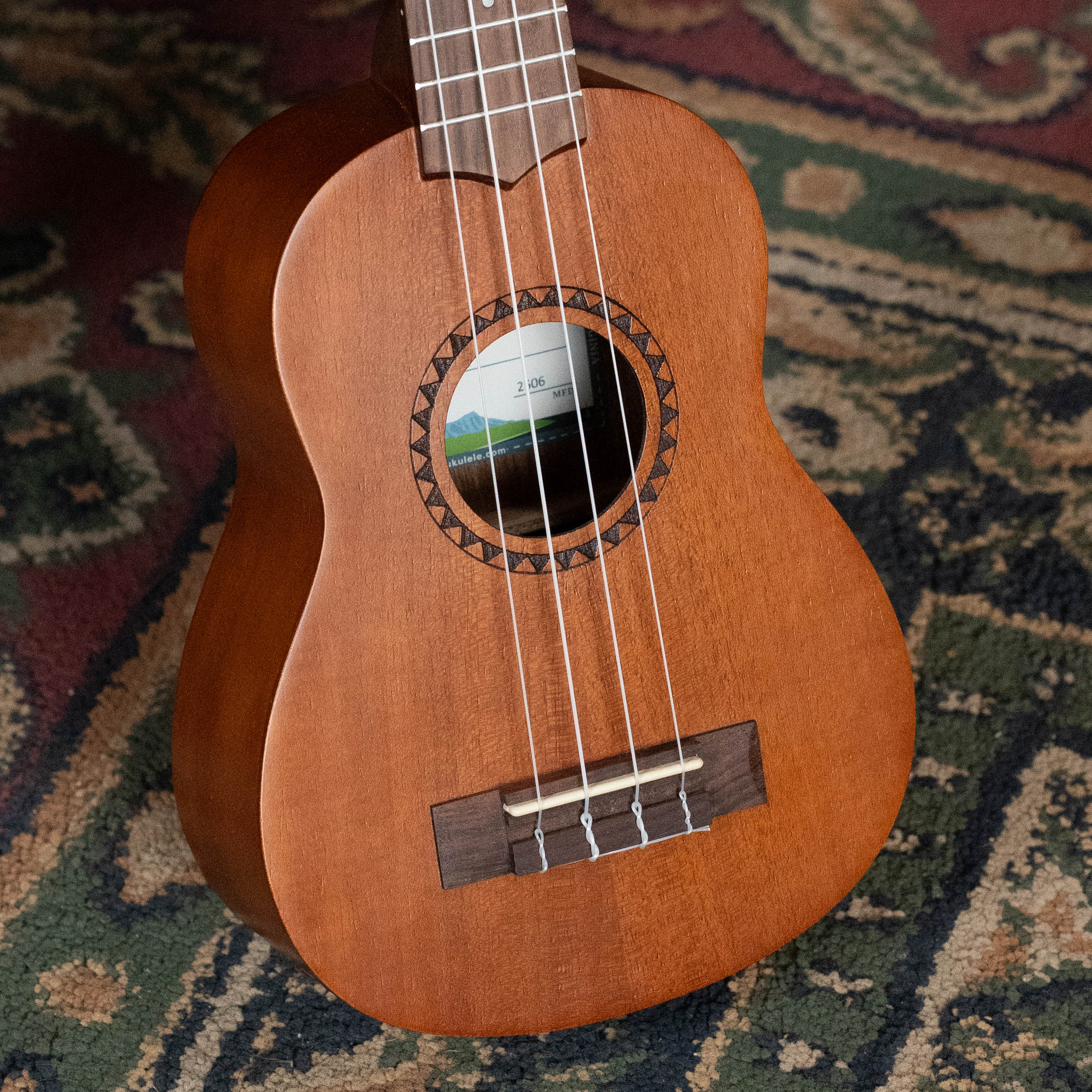 Soprano ukulele with satin mahogany body, rosewood bridge, and four nylon strings on patterned rug background. - Kala KA-15S Satin Mahogany Soprano Ukulele - Default Title
