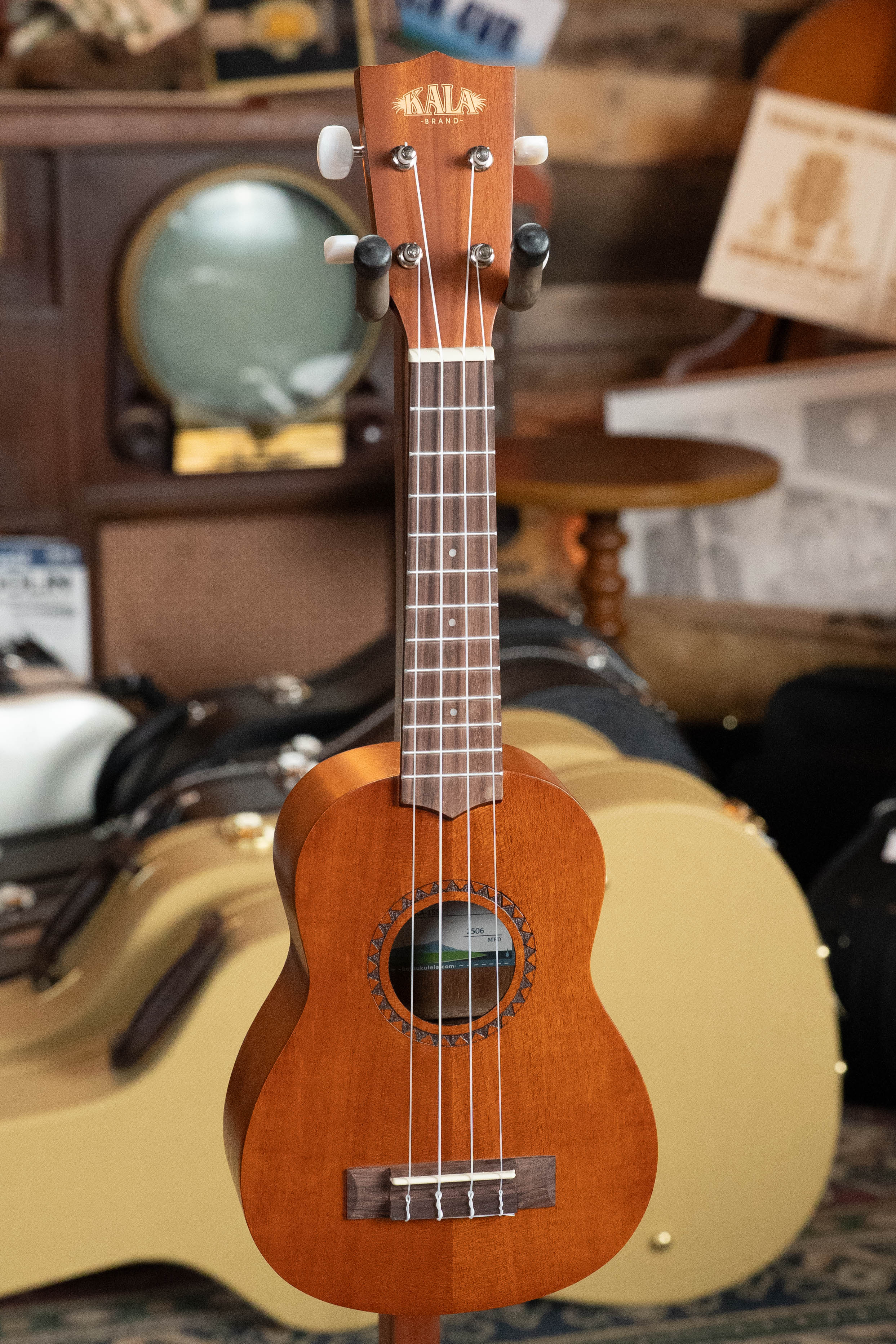 Satin mahogany soprano ukulele with dark fretboard and silver tuning pegs on wooden stand. - Kala KA-15S Satin Mahogany Soprano Ukulele - Default Title