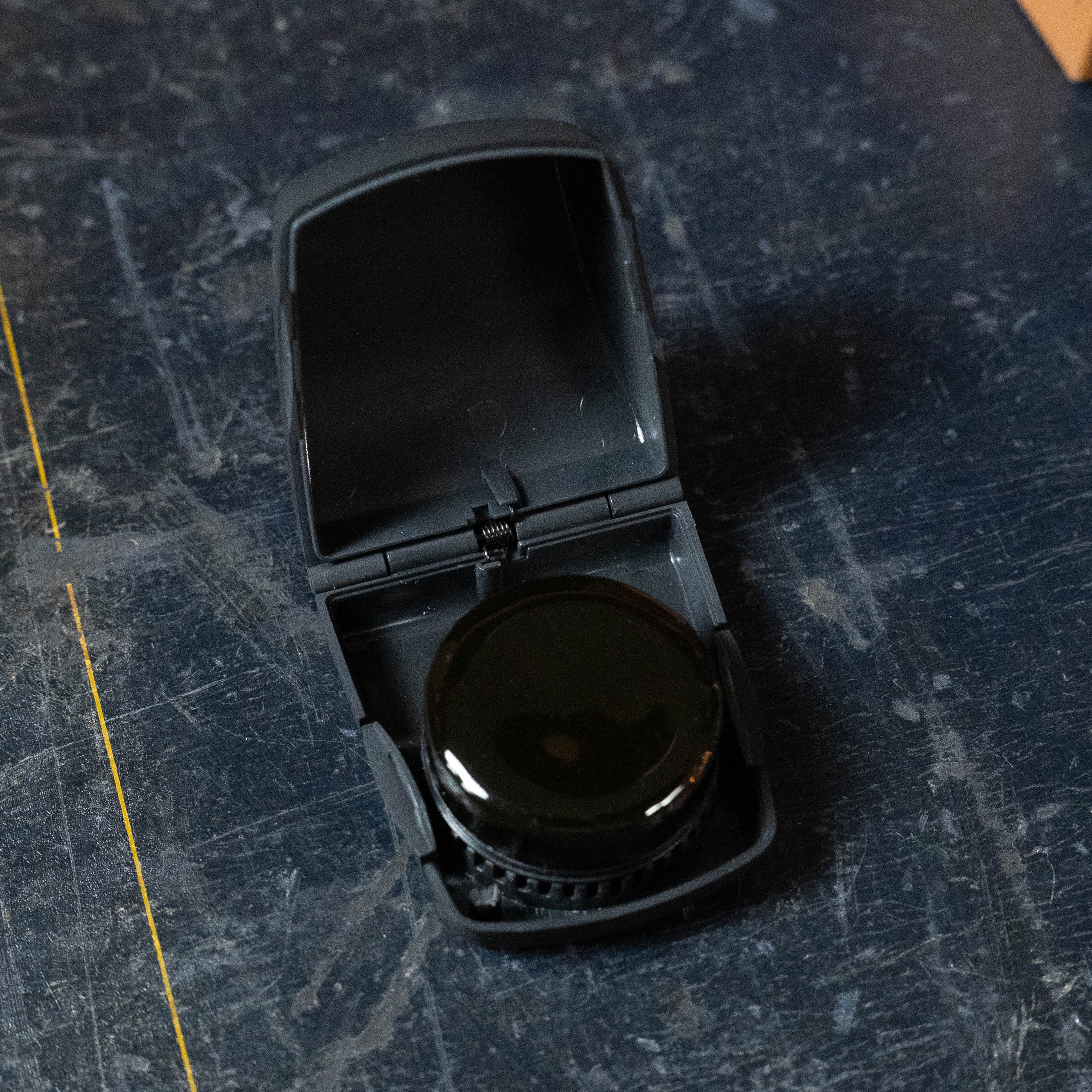 A black plastic case rests open on a dark surface, showing a round black D'Addario Kaplan Premium Rosin (KRD) inside—favored by violinists for its low dust and high quality.