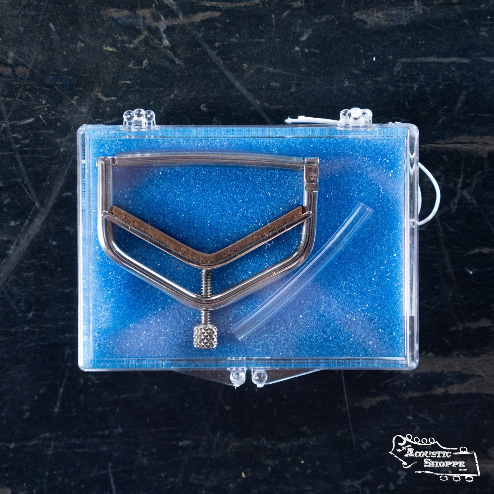A Kat Eyz Stainless Steel 12 Radius Guitar Capo (1/4 TS) is displayed in a clear plastic case lined with blue foam. The handmade capo rests on a dark surface, with the “Acoustic Shoppe” logo visible in the bottom right corner.