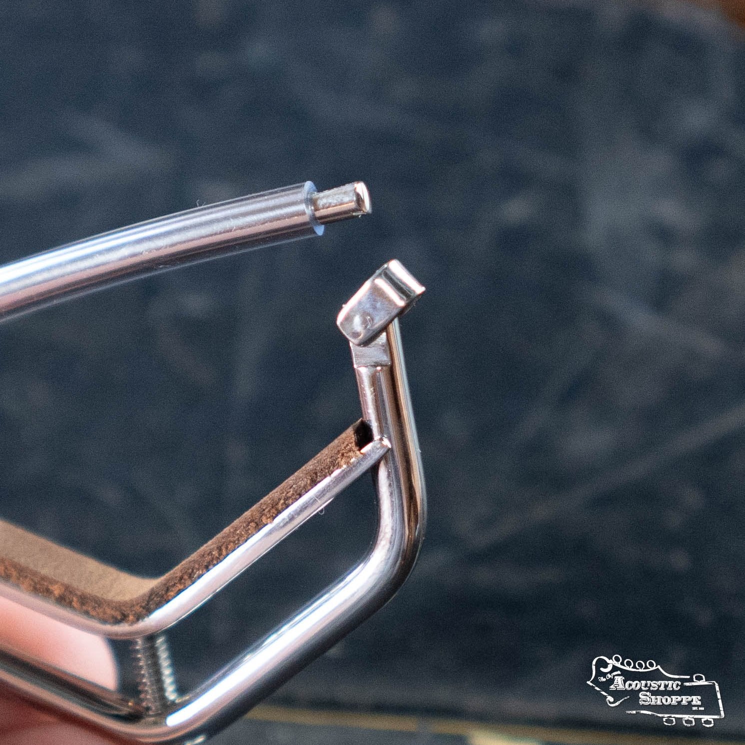 A close-up of a damaged Kat Eyz Stainless Steel 12 Radius Guitar Capo (1/4 TS), missing a protective tip on one arm, with a broken end piece, set against a blurred dark background.