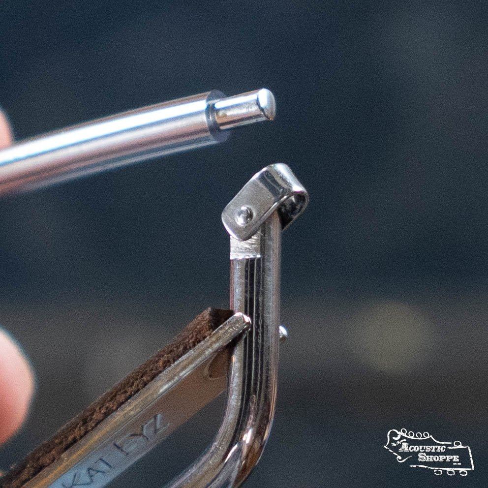A close-up of a pen tip pointing at the hinge of a Kat Eyz Stainless Steel 16 Radius Guitar Capo (1/4 TS), with a blurred background and the Acoustic Shoppe logo in the corner.