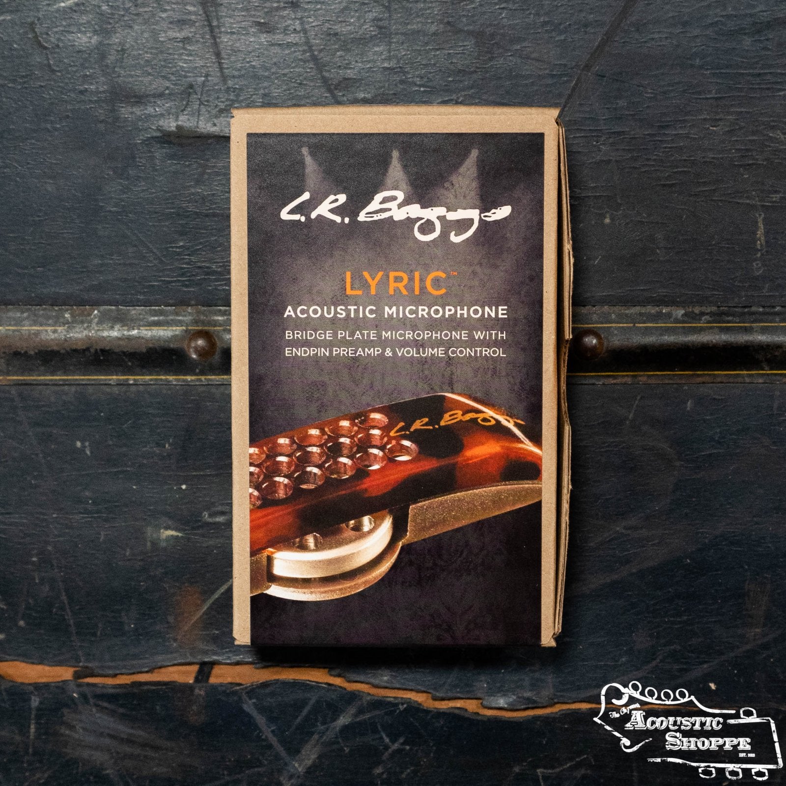A boxed L.R. Baggs Lyric Acoustic Guitar Microphone rests on a dark wooden surface. The packaging highlights the mic’s features, including TRU•MIC technology, and displays The Acoustic Shoppe logo in the corner.