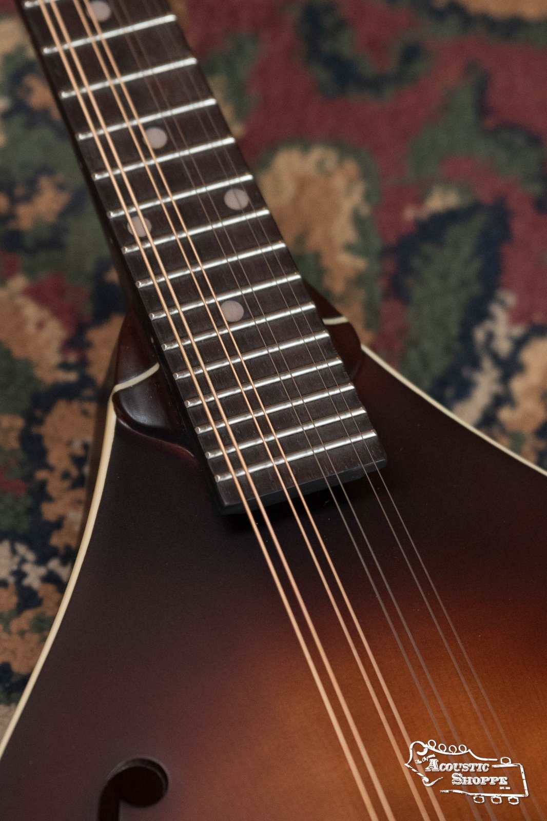 Close-up of The Loar LM-110E-BRB "Honey Creek" A-Style Brownburst Mandolin w/Pickup #0688 fretboard and spruce top on a patterned carpet, with the “Acoustic Shoppe” logo in the bottom right corner.