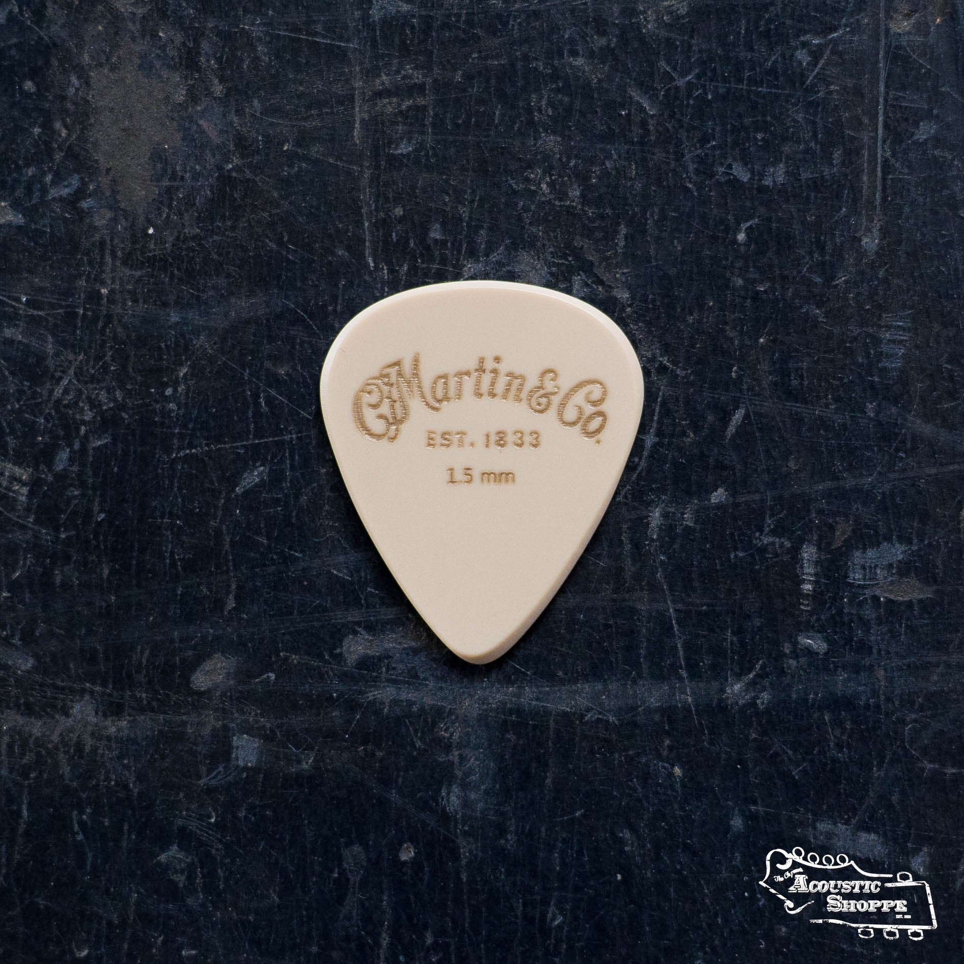 A LUXE By Martin Apex Pick - 1.5mm by Martin & Co., made from wear-resistant polymer, rests on a dark textured surface with The Acoustic Shoppe logo in the lower right corner.
