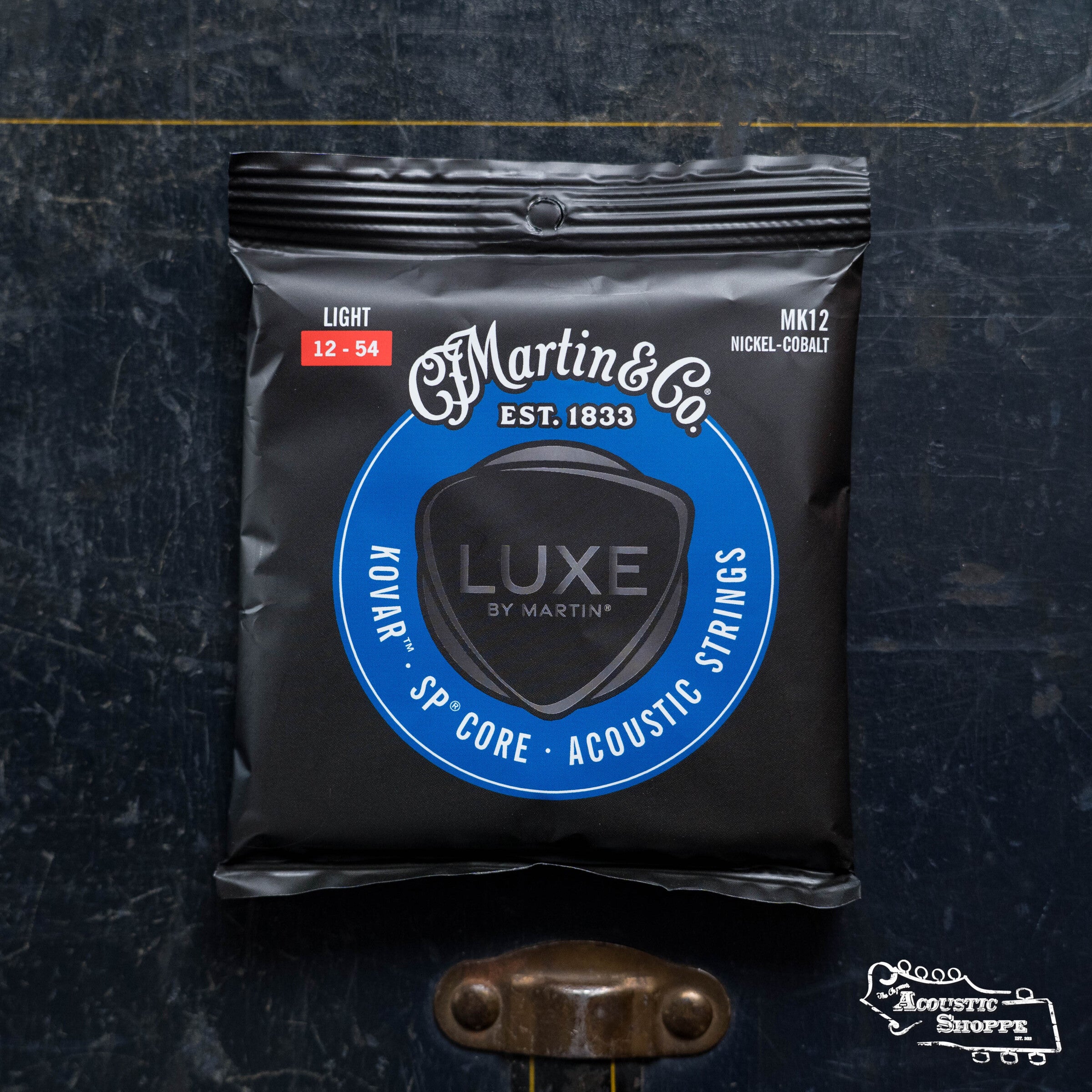 A package of LUXE By Martin Kovar Light Strings 41Y23MK12 by Martin & Co., featuring Light 12-54 gauge nickel-cobalt alloy, rests on a dark surface with the Acoustic Shoppe logo in the lower right corner.