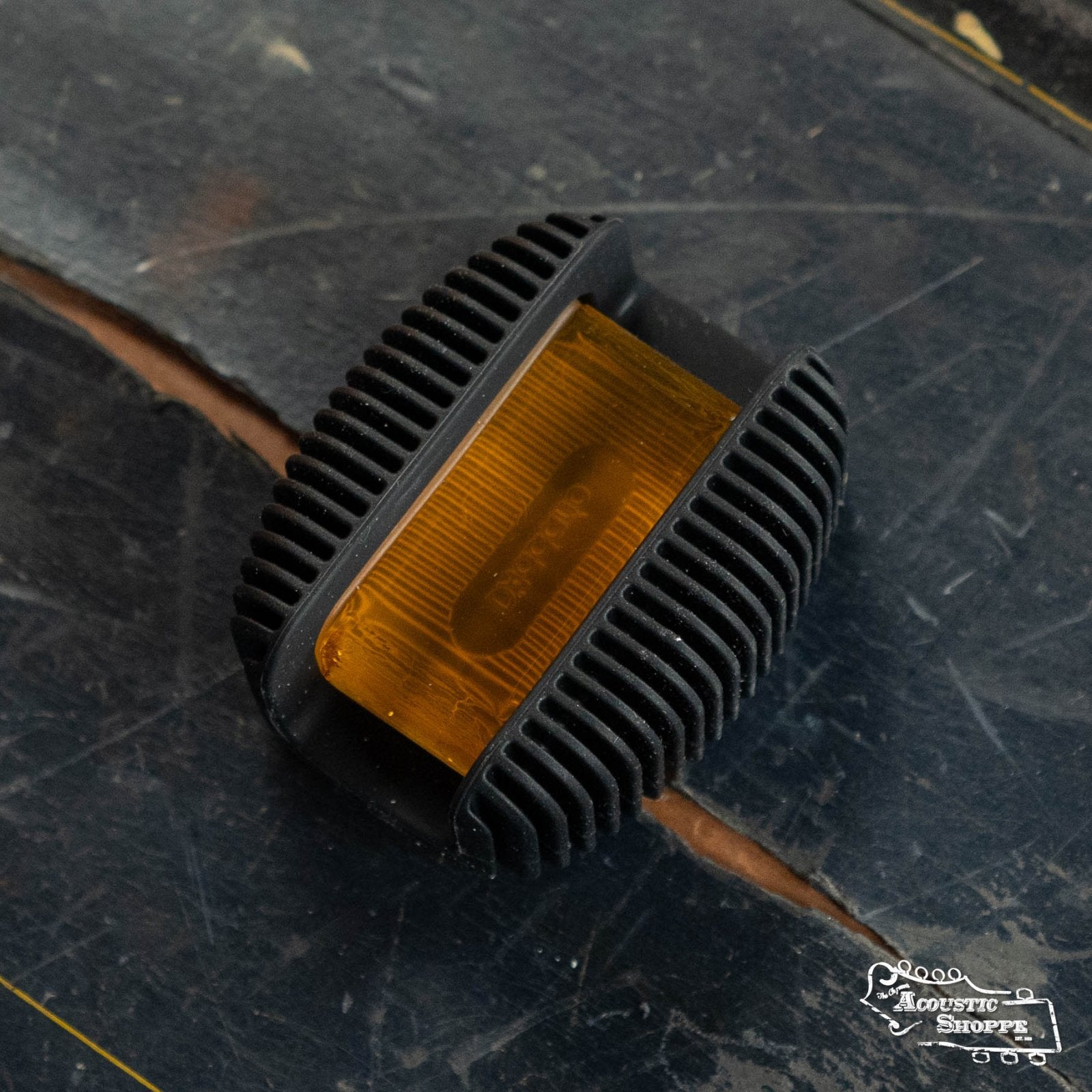 A close-up of the DAddario DRGBK-VR200 Rosin Guard with Natural Light Rosin, featuring amber rosin in a black, ribbed grip, resting on dark wood. The Acoustic Shoppe logo appears in the bottom right corner.