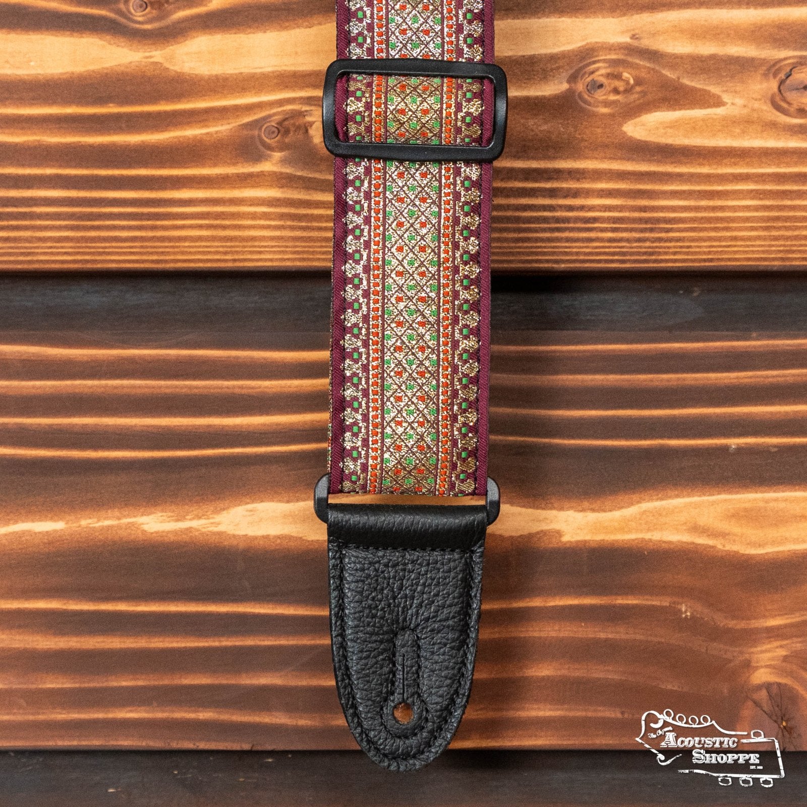 Levy's Leather 2” Woven Strap (M8TF-001) features a burgundy Thai motif jacquard top with gold and green accents, black adjustable buckle, and black leather ends, shown on a rustic wooden background.