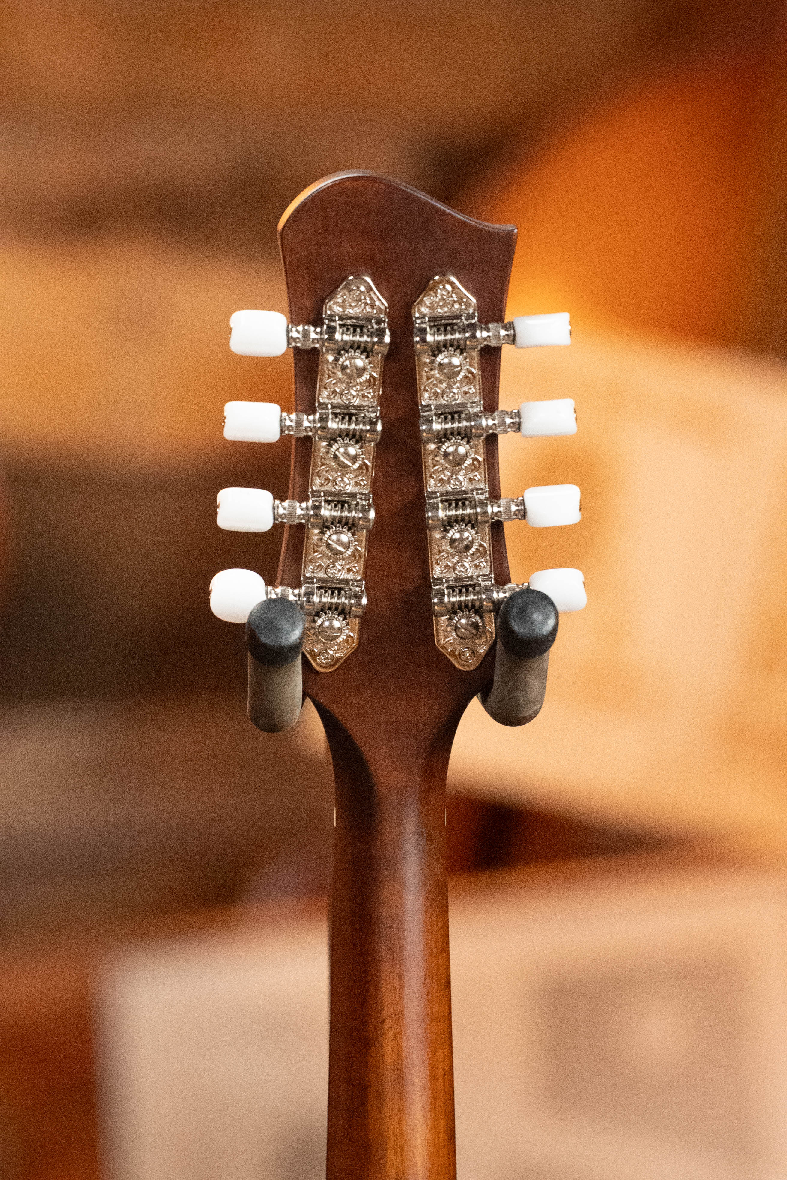 Close-up of the Eastman Guitars MD305 Spruce/Maple A-Style Hand-Carved Mandolin #3317 headstock, displaying ornate silver tuners with white pegs on a wooden neck, set against a softly blurred background.