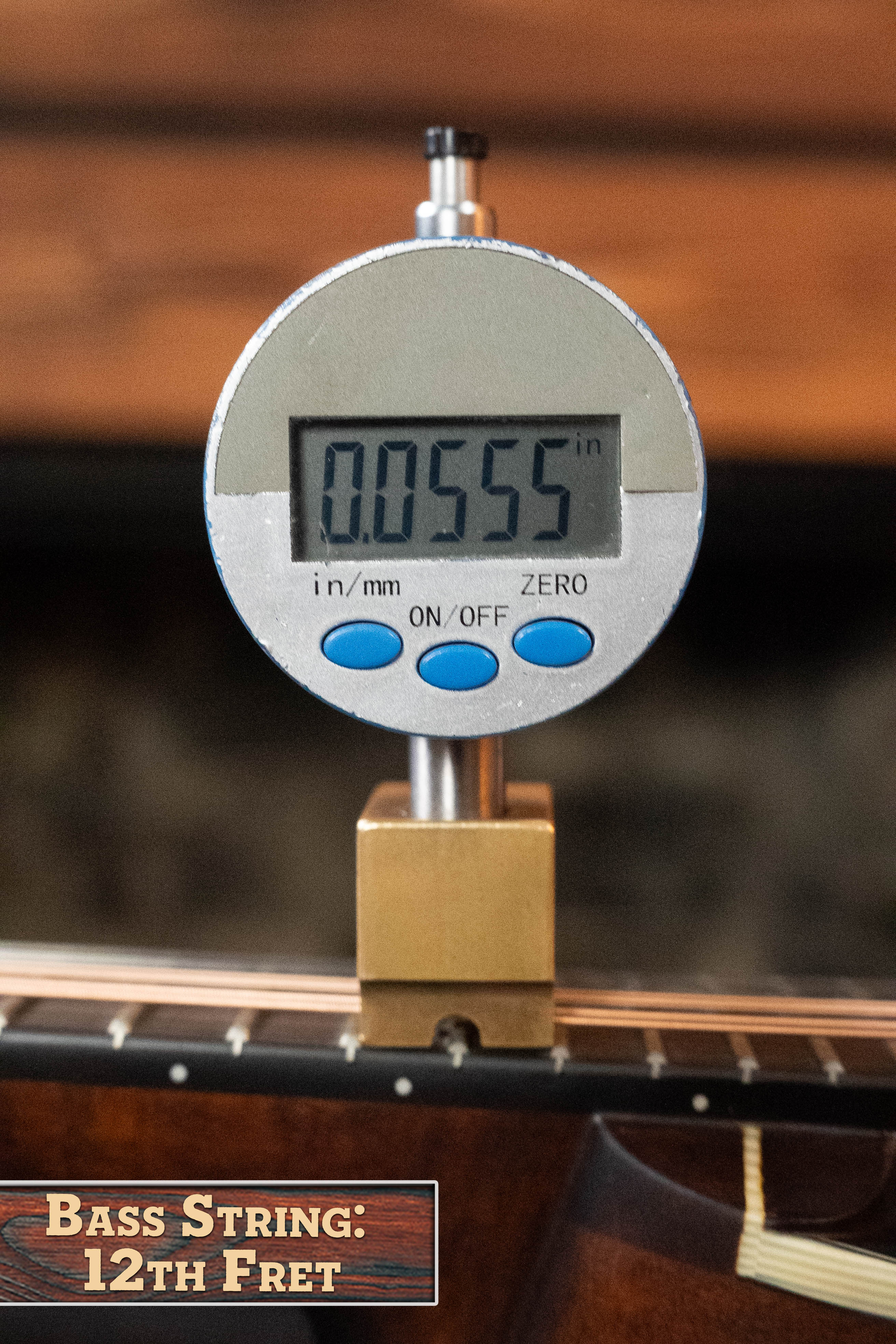 A digital gauge shows 0.0555 inches for a bass string at the 12th fret. Nearby, a sign reads "BASS STRING: 12TH FRET" next to an Eastman Guitars MD305 A-Style Hand-Carved Mandolin #3317 with a solid spruce top on display.