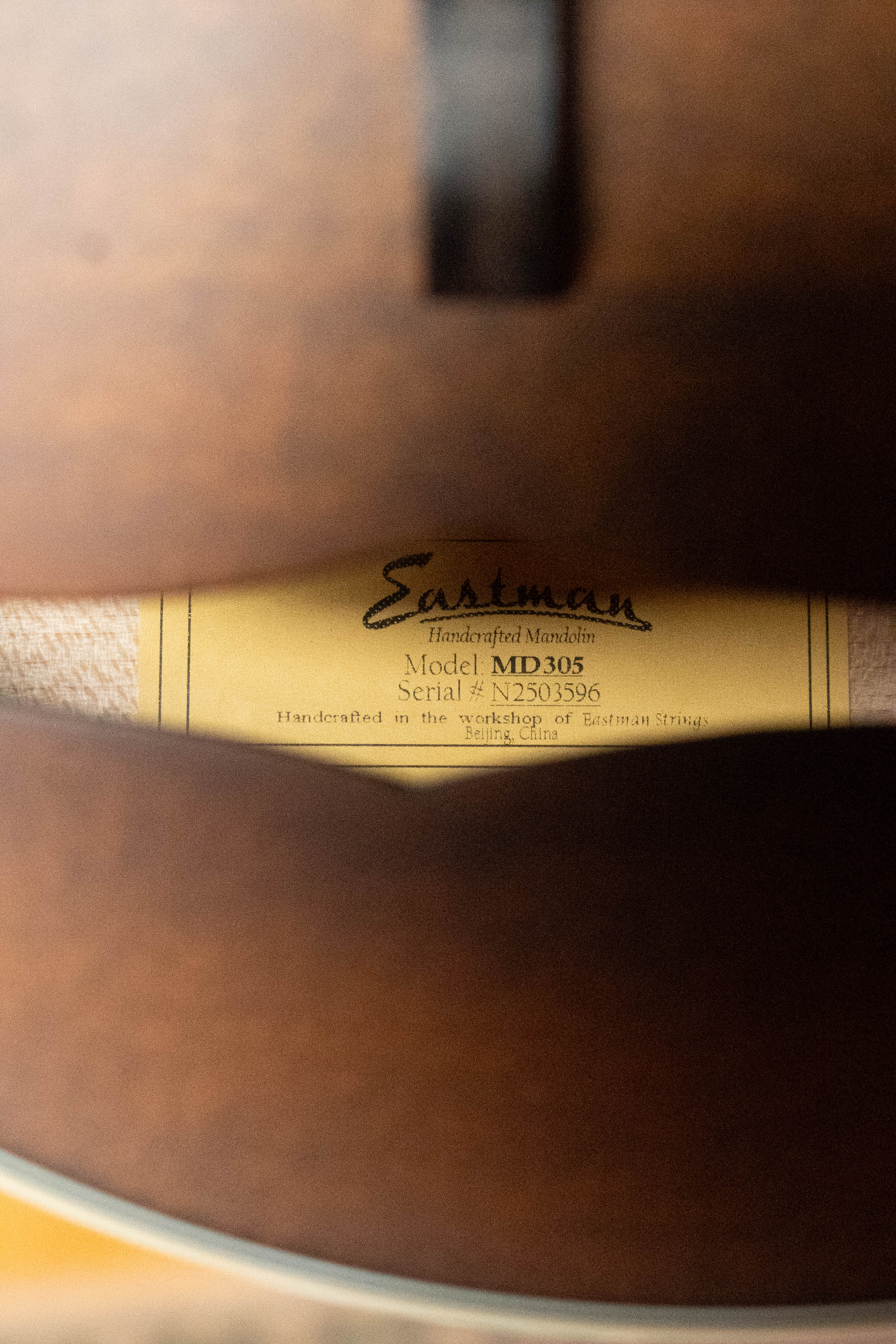 A close-up through the F-hole of an Eastman Guitars MD305 Spruce/Maple A-Style Hand-Carved Mandolin (#3596) shows its inside label, handcrafted in Beijing, China.