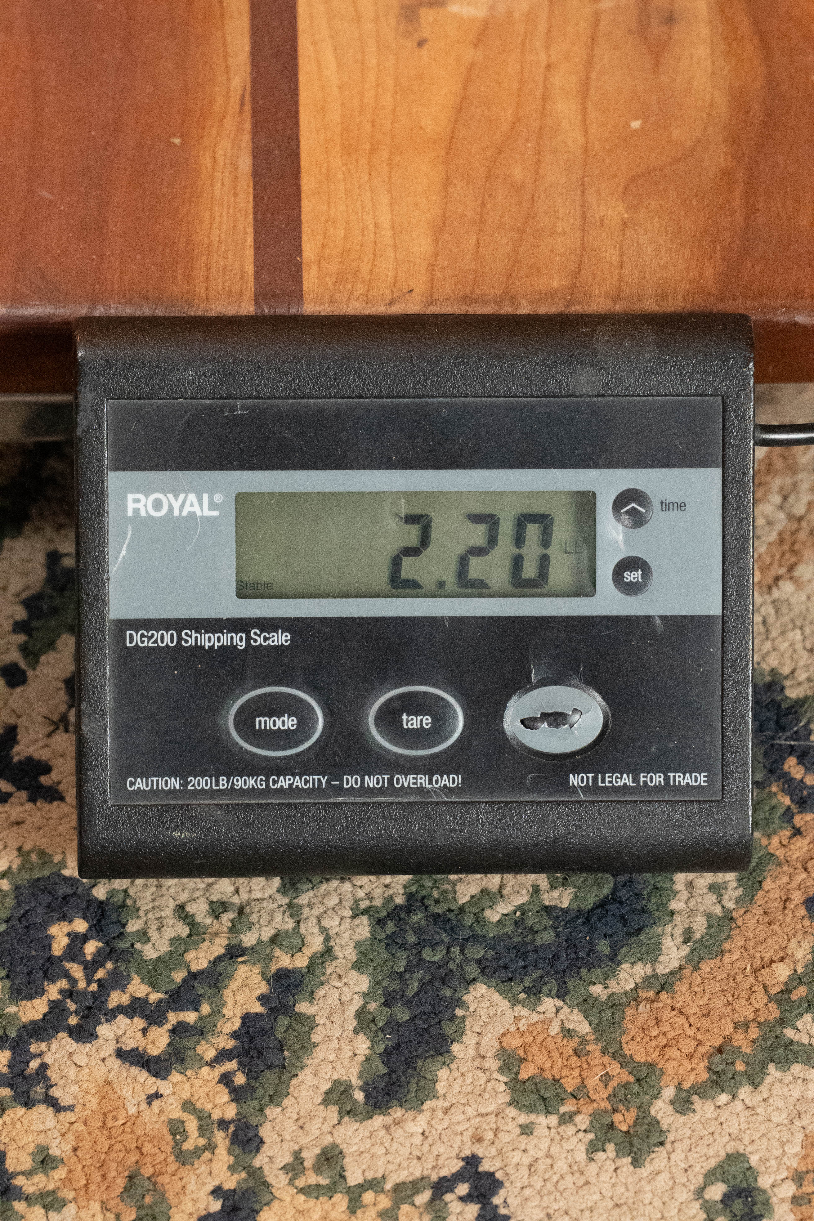 An Eastman Guitars MD305 Spruce/Maple A-Style Hand-Carved Mandolin (#3596) rests partly on a digital shipping scale atop a patterned carpet, displaying a weight of 2.20 pounds near the scale’s 200 lb/90 kg capacity warning label.