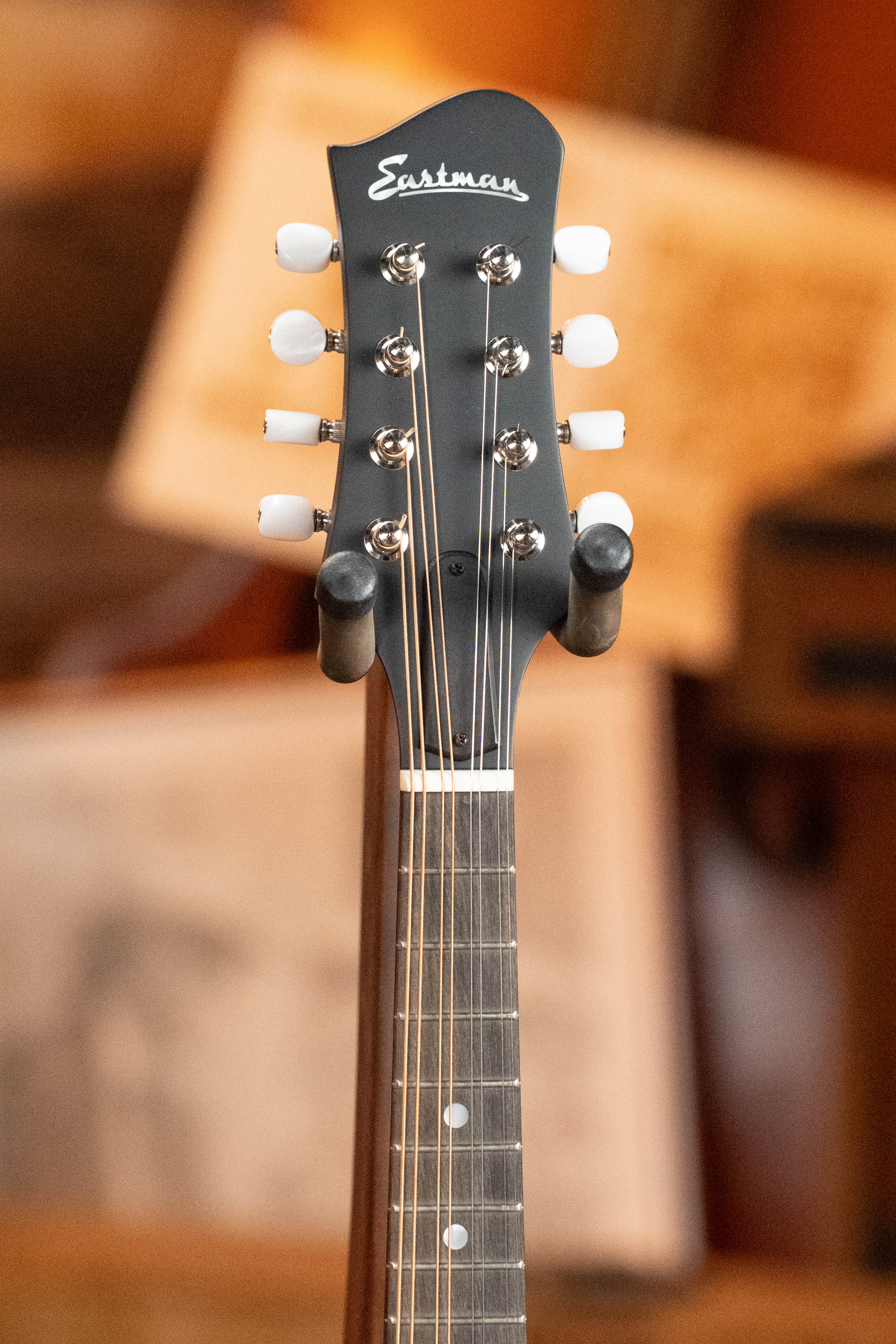 Close-up of the Eastman Guitars MD305 Spruce/Maple A-Style Hand-Carved Mandolin #3596 headstock, featuring tuning pegs, strings, and Eastman logo against a softly blurred background showcasing its craftsmanship.