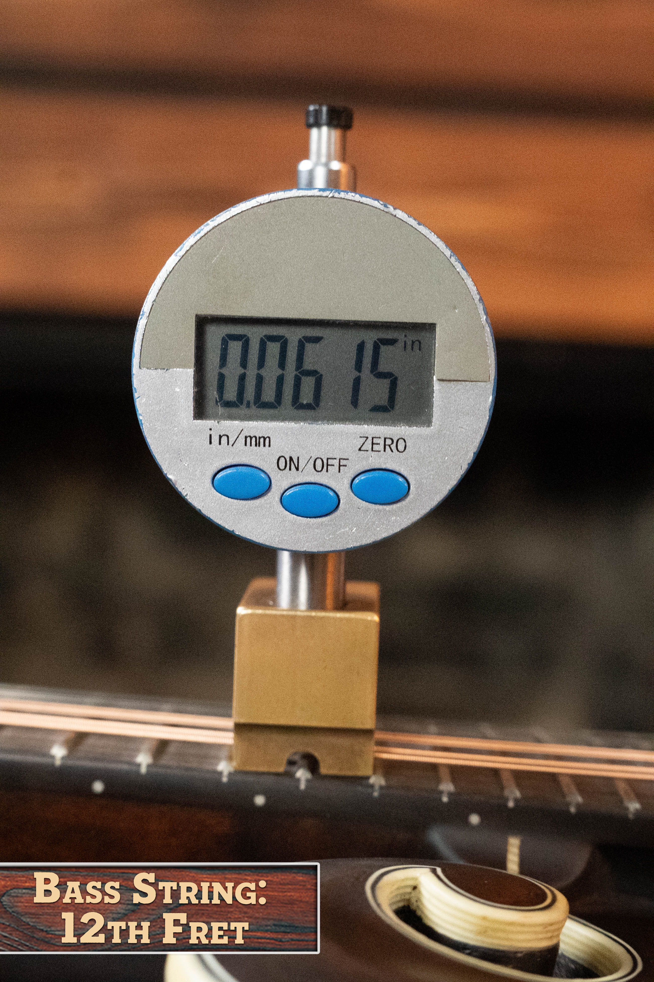 A digital caliper measures 0.0615 inches of string height above the 12th fret of a bass guitar. The label reads "Bass String: 12th Fret," similar to checking action on an Eastman MD315 F-Style Hand-Carved Mandolin by Eastman Guitars.