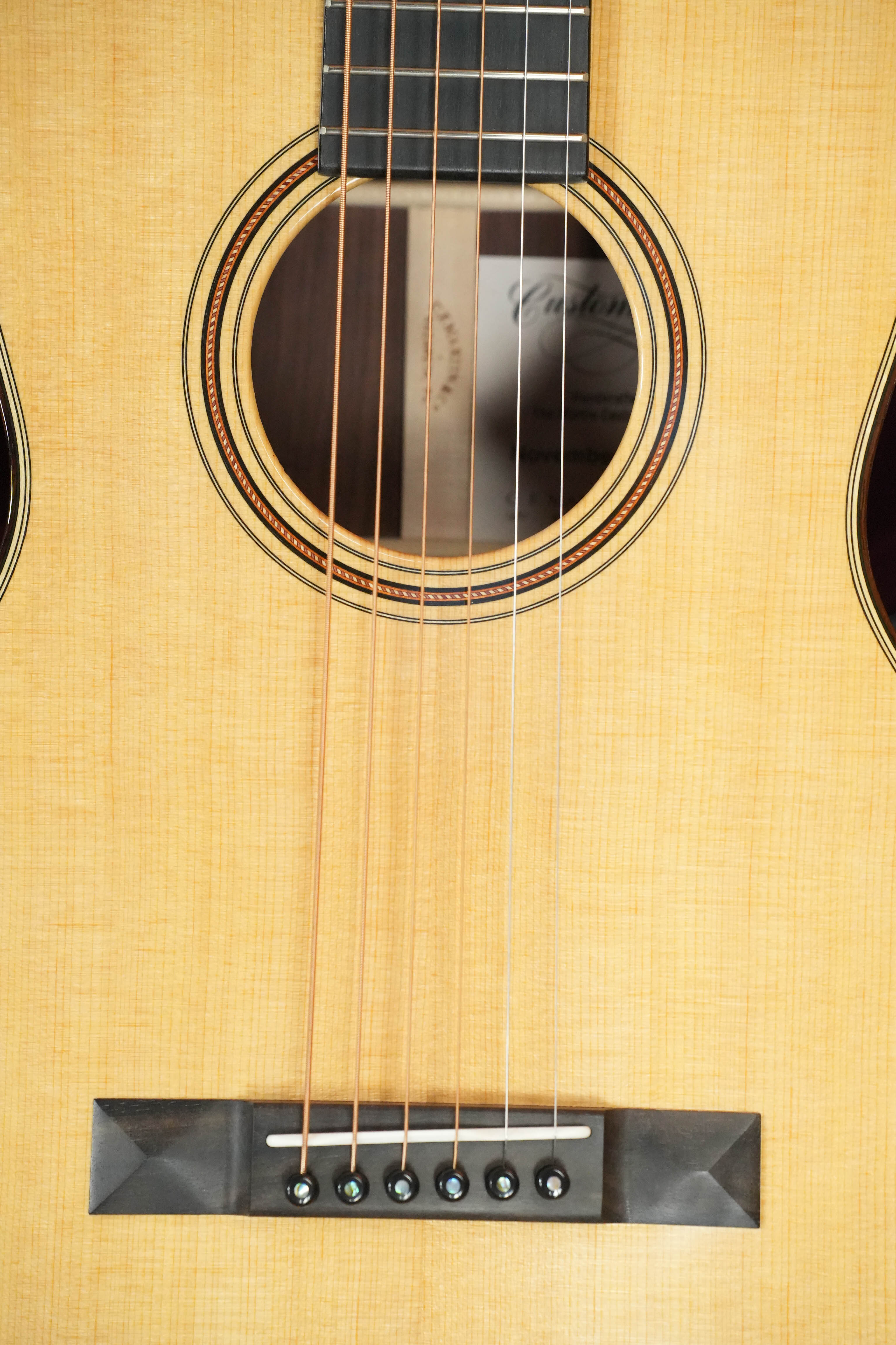Close-up of a Martin & Co. Custom Shop Sitka/Rosewood Acoustic Guitar #6904 body, showcasing six strings, a decorative rosette sound hole, and a Guatemalan rosewood bridge with six pins securing the strings.