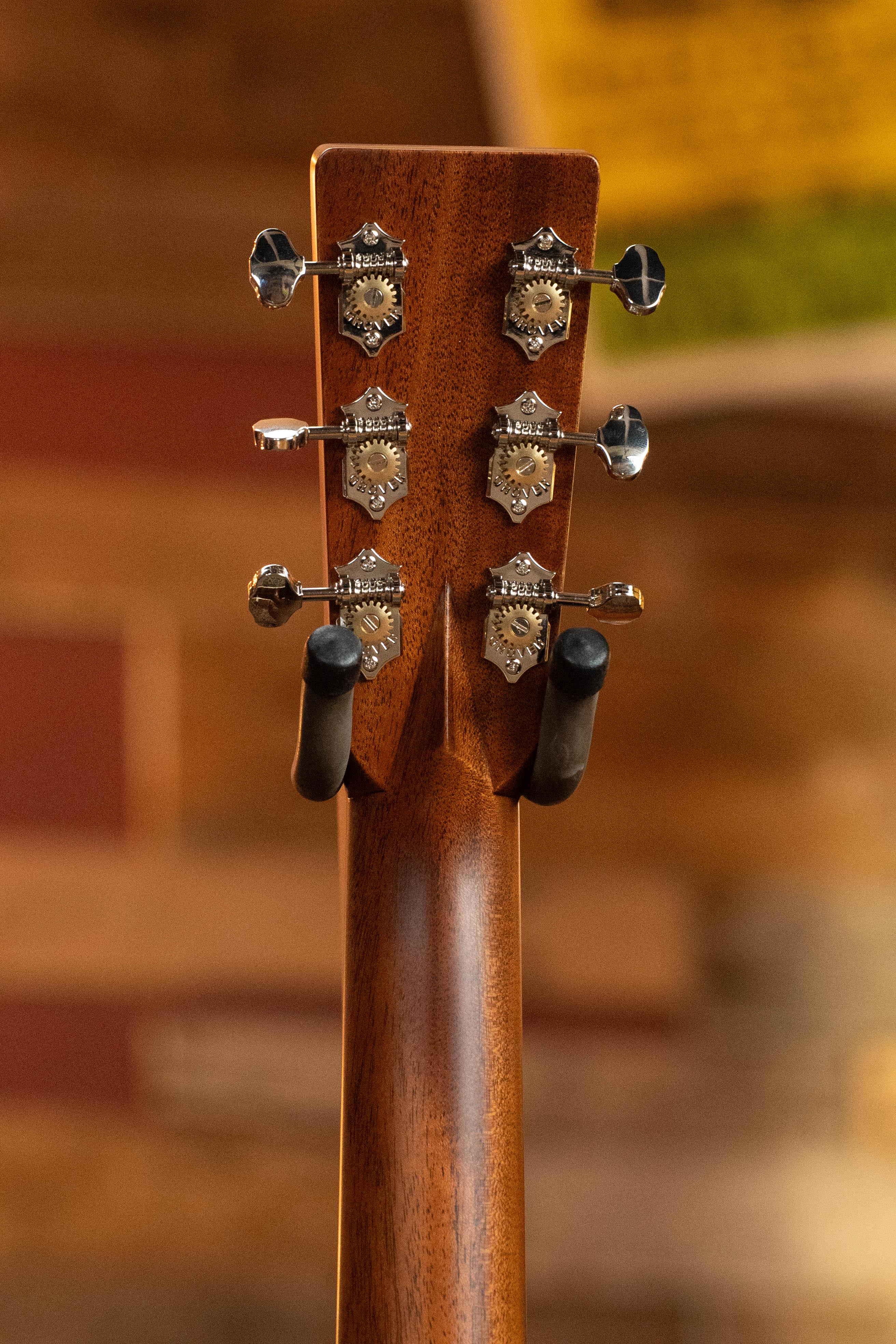 Close-up of the Martin & Co. Custom Shop HD-28 Style Spruce/Wild Grain Rosewood "D" Dreadnought Acoustic Guitar #7410 headstock, with six silver tuners and gears, mounted on a black hanger against a warm wooden background.