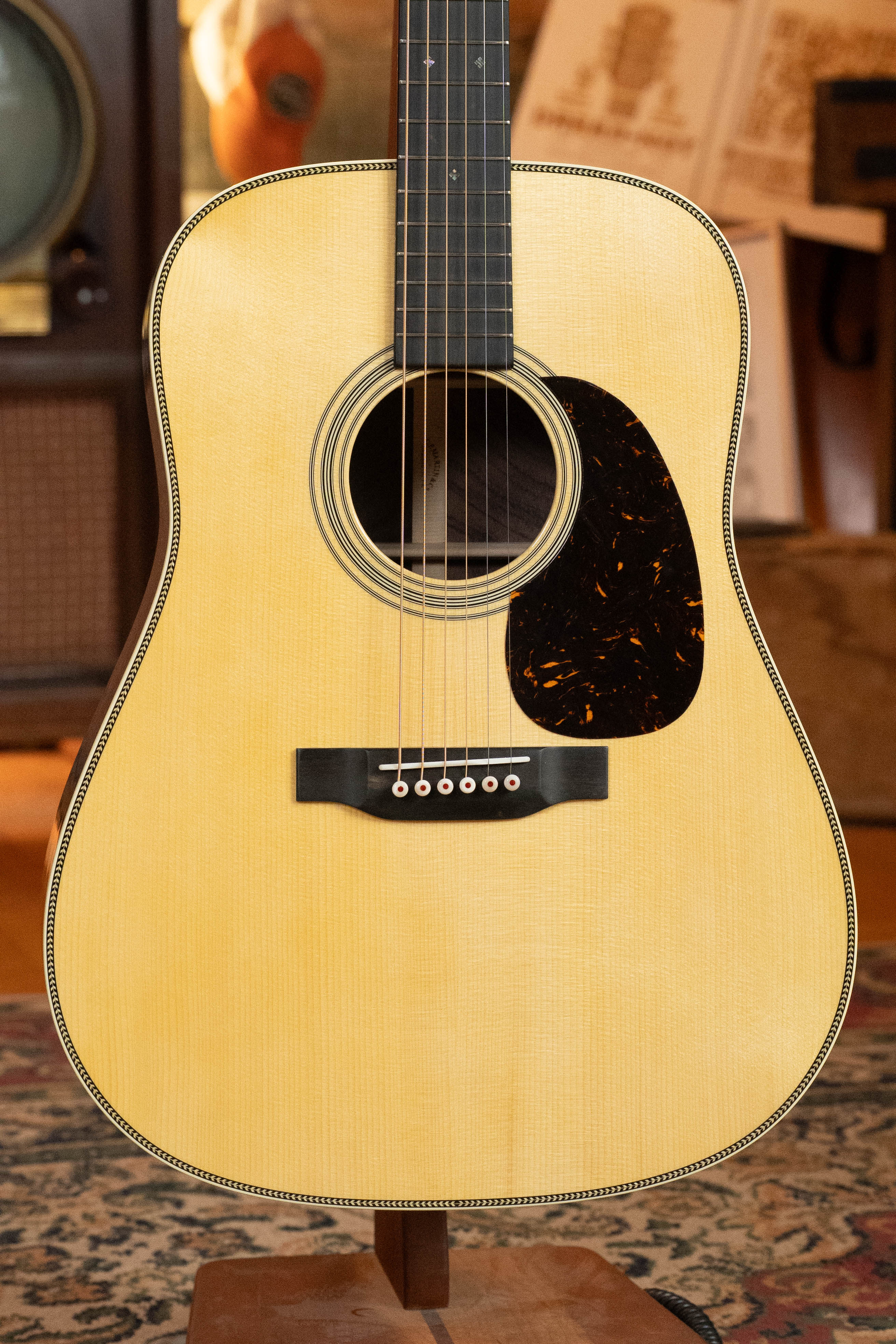 A close-up of the Martin & Co. Custom Shop HD-28 Style "D" Dreadnought Acoustic Guitar #7410, featuring a light Adirondack spruce top, black pickguard, and six strings, set indoors with vintage decor in the background.