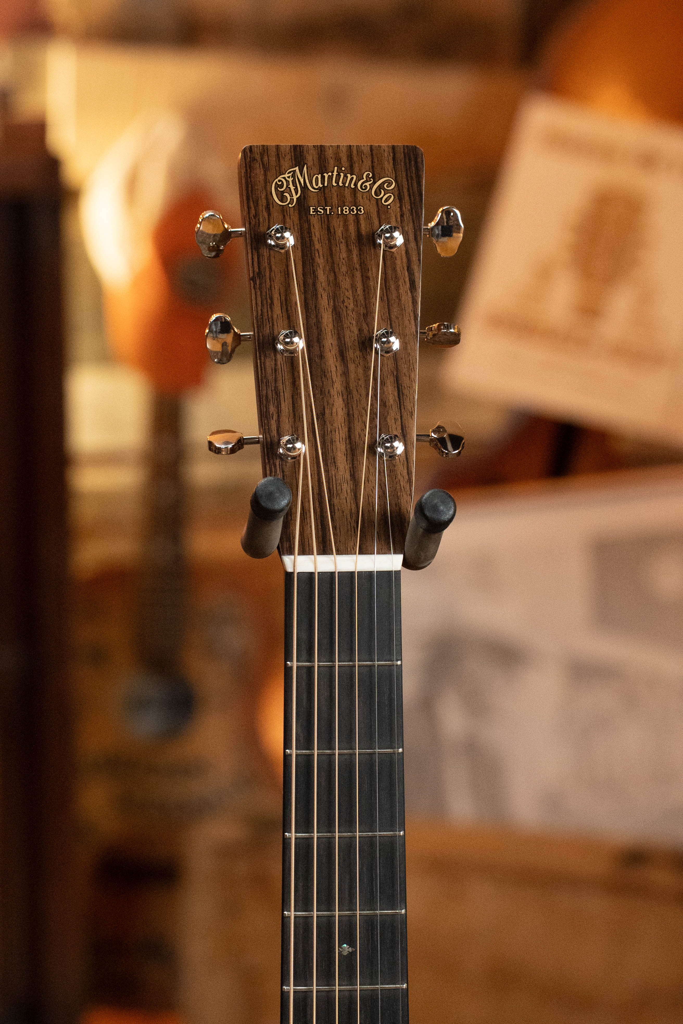 Close-up of the headstock of a Martin & Co. Custom Shop HD-28 Style Spruce/Wild Grain Rosewood Custom "D" Dreadnought Acoustic Guitar #7410, featuring tuning pegs and strings against a blurred, warm-toned background.