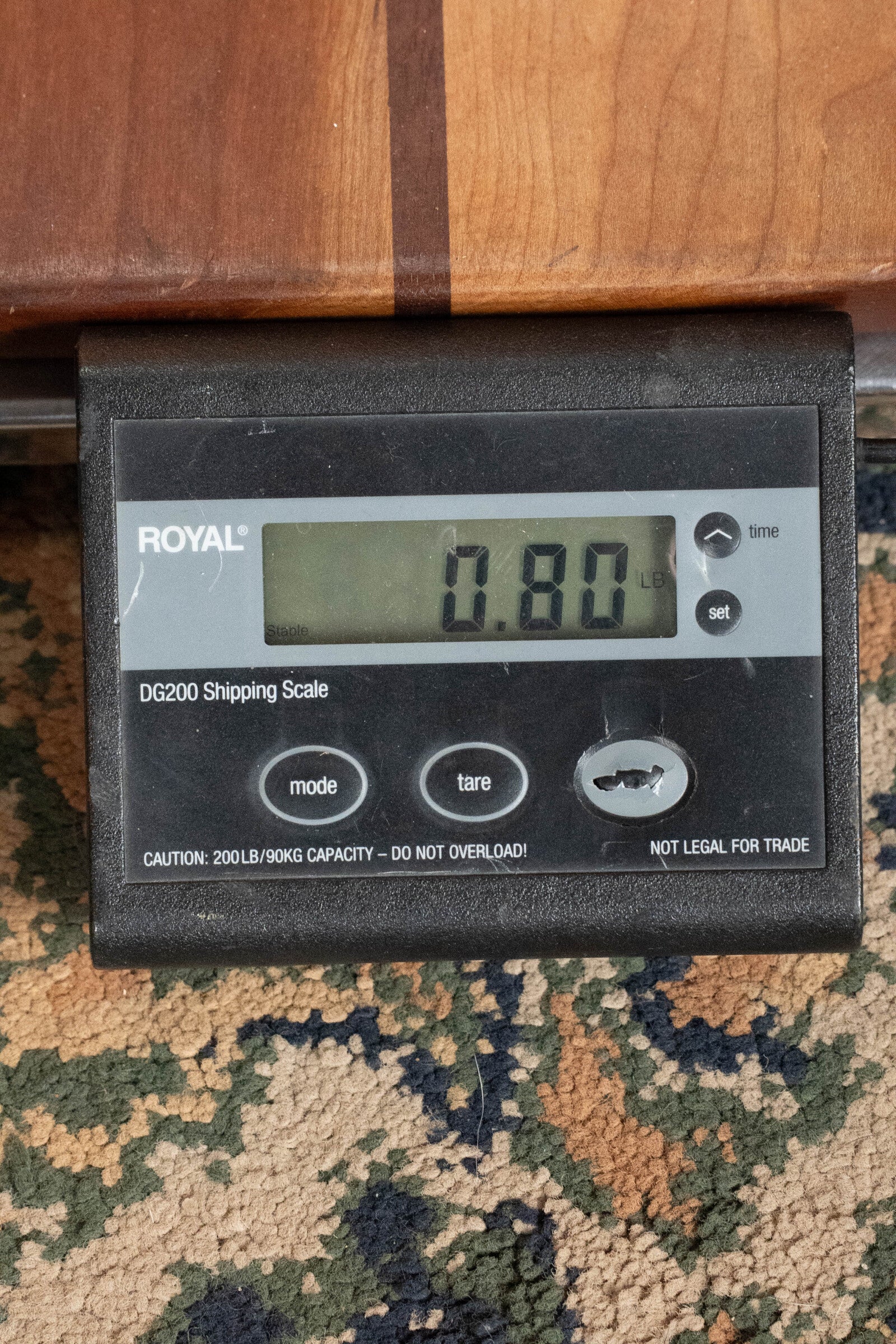 A digital shipping scale displays 0.80 lbs as a Martin & Co. Centennial Concert All Mahogany Ukulele (#8239) rests on it atop a patterned carpet with a wooden surface visible above.