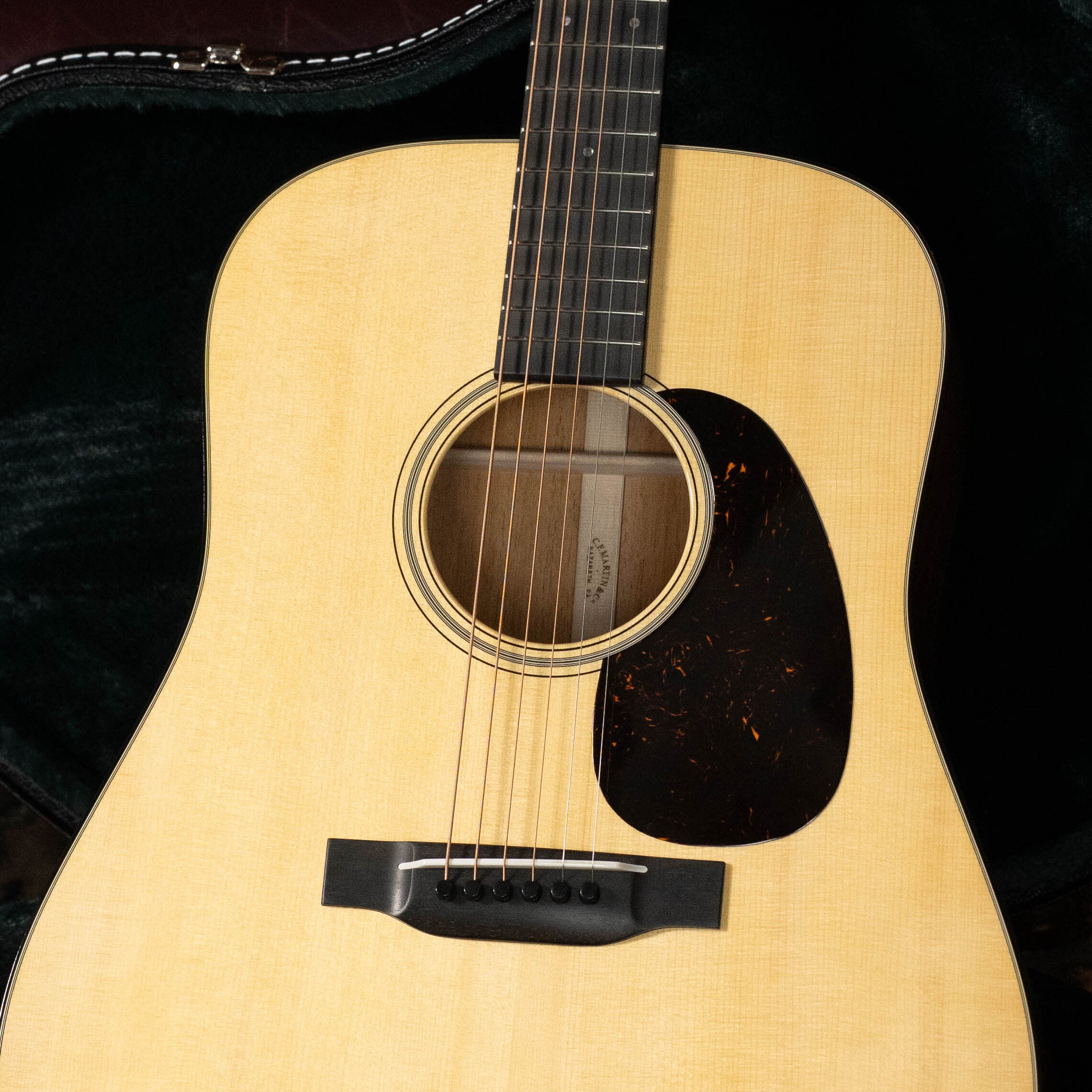 A close-up of the Martin & Co. Custom Shop D-18V Adirondack/Mahogany Dreadnought Acoustic Guitar #6905, showing its Adirondack spruce top, black pickguard, and visible strings as it rests in a dark, plush-lined guitar case.