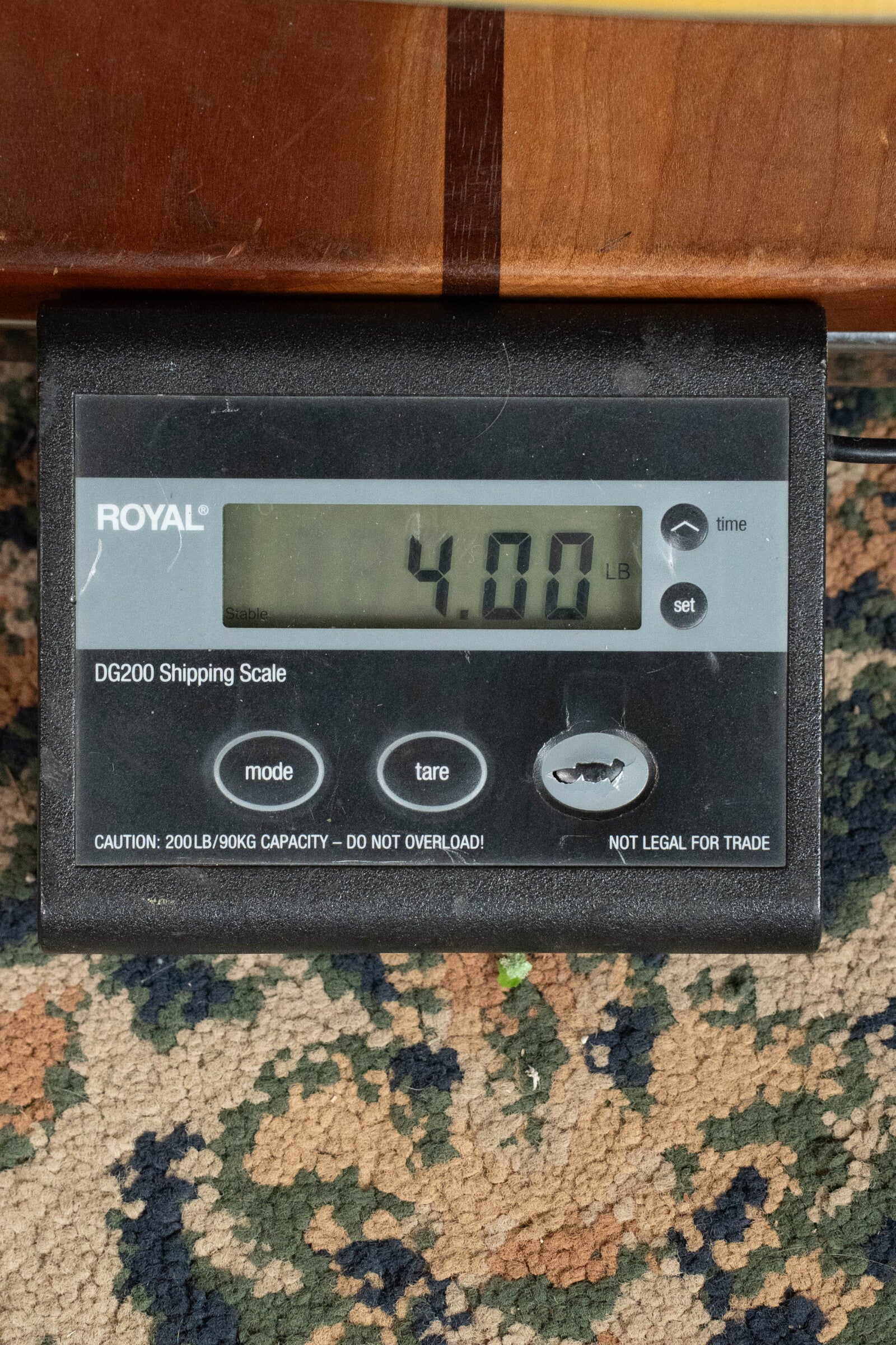 A digital shipping scale reads 4.00 pounds, likely the weight of a Martin & Co. Custom Shop D-18V Adirondack/Mahogany Dreadnought Acoustic Guitar #6905. The patterned carpet and labeled buttons are visible along with a capacity caution.
