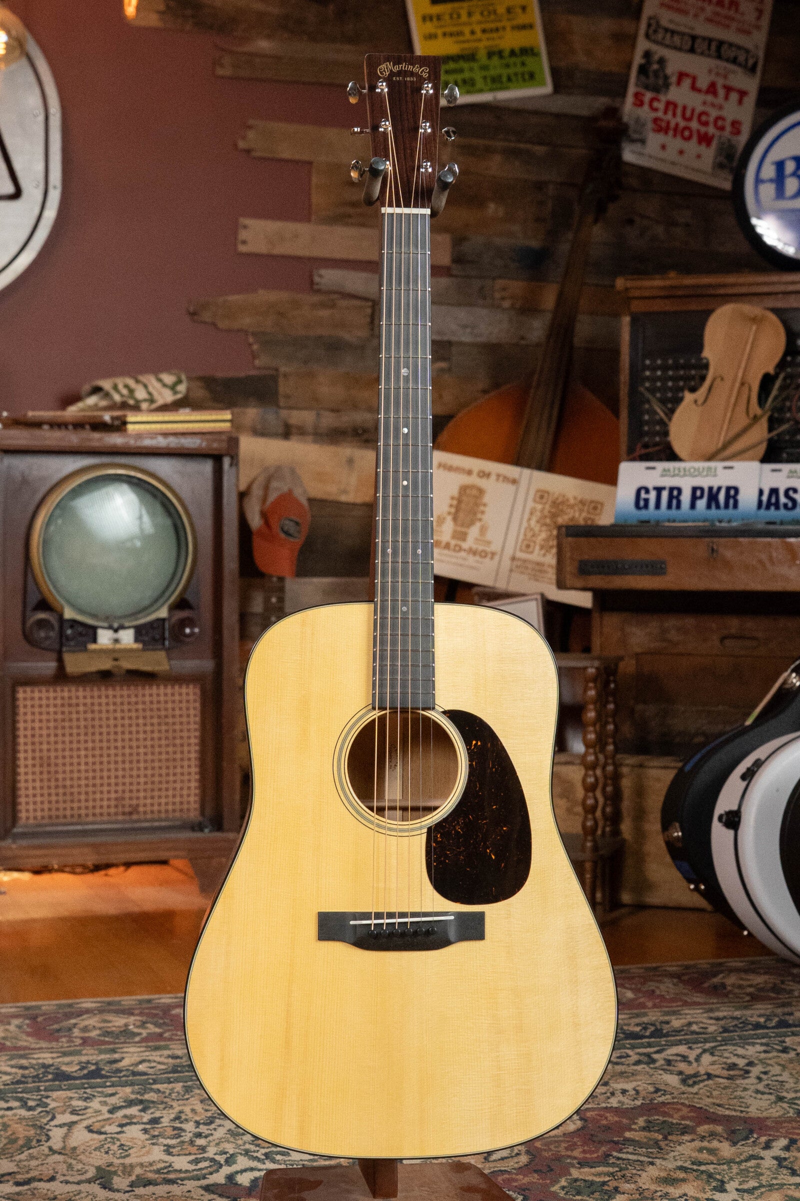 The Martin & Co. Custom Shop D-18V Adirondack/Mahogany Dreadnought Acoustic Guitar #6905, with a light wood body and dark pickguard, stands upright in a cozy, retro-style room filled with vintage musical charm.
