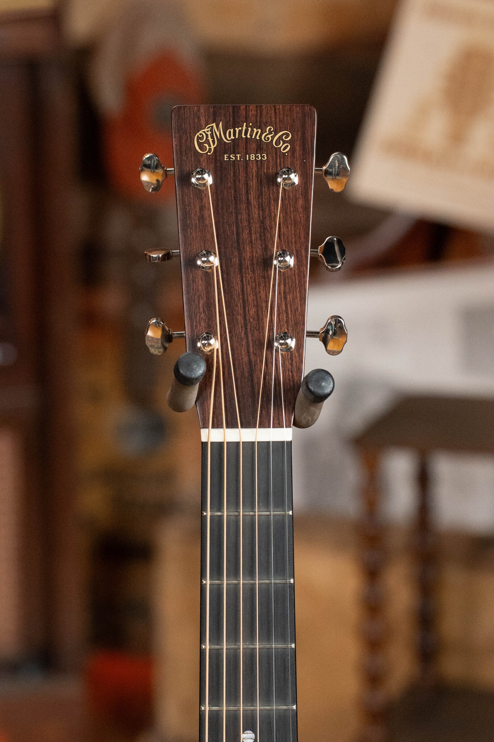 Close-up of the Martin & Co. logo and tuning pegs on the headstock of a Martin Custom Shop D-18V Adirondack/Mahogany Dreadnought Acoustic Guitar #6905, set against a blurred, warm-toned background—an elegant vintage detail.